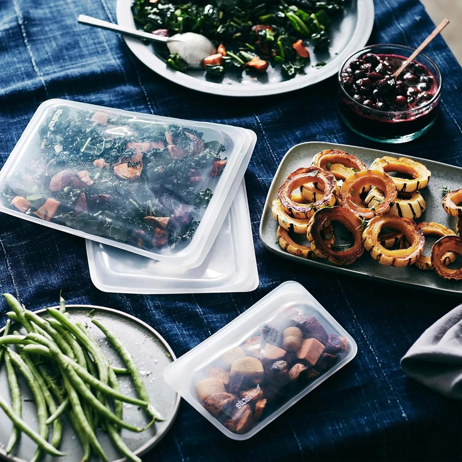 multiple stasher bags on a table with various dishes and bowls of food
