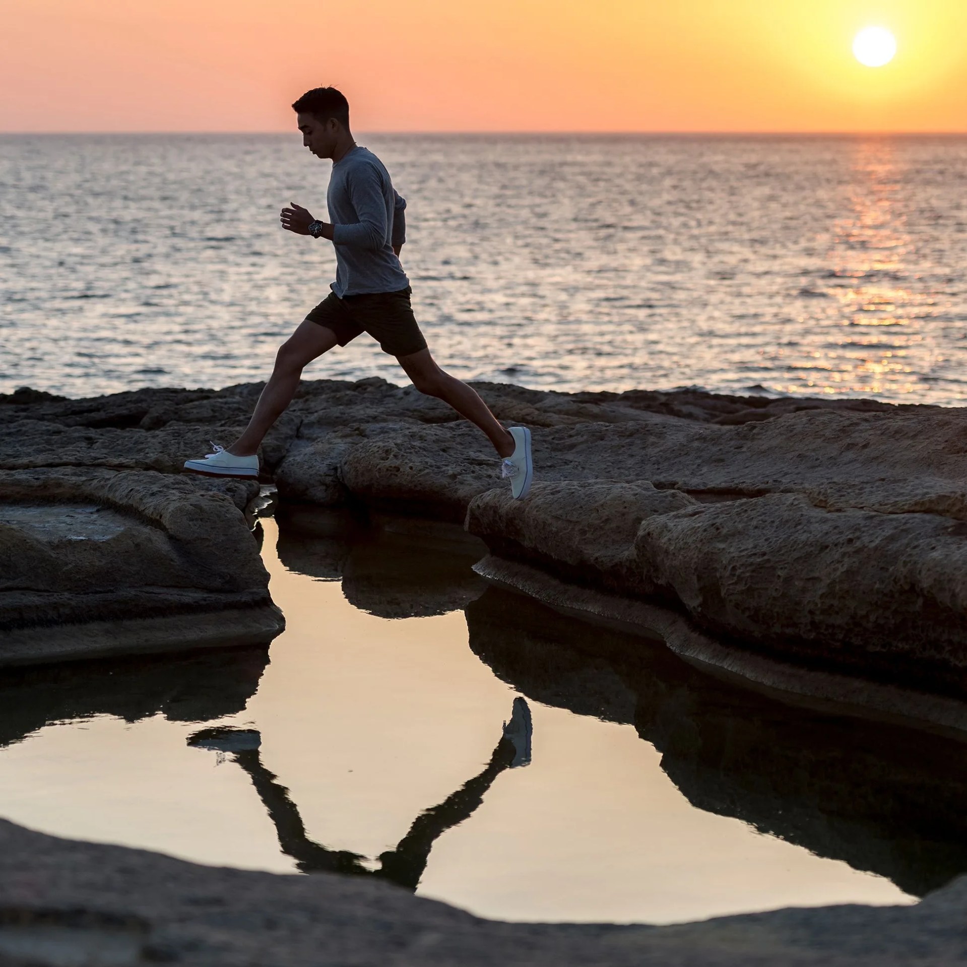 man hoping across rocks during sunset