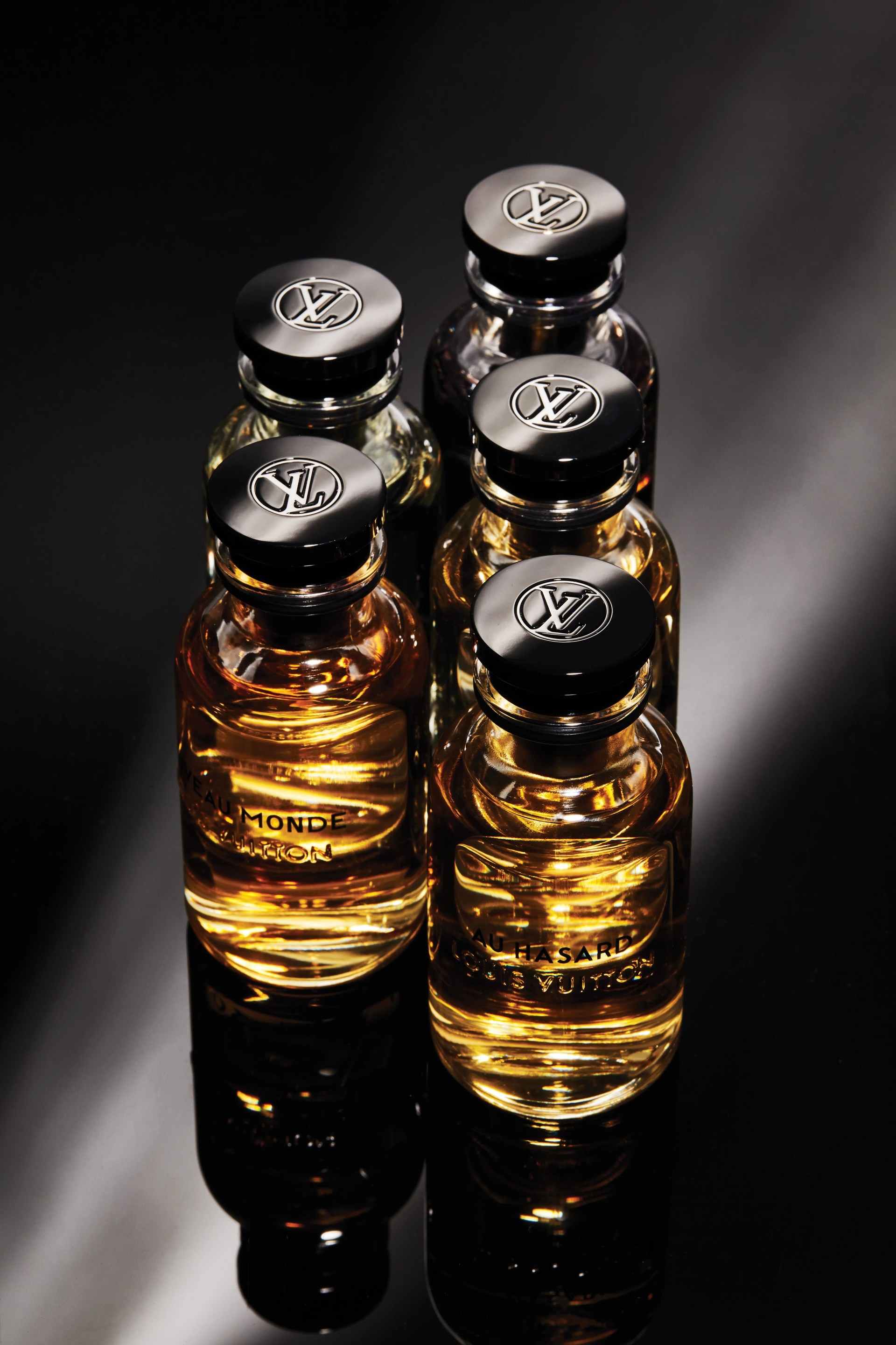 five bottles of louis vuitton cologne laying on a dark surface
