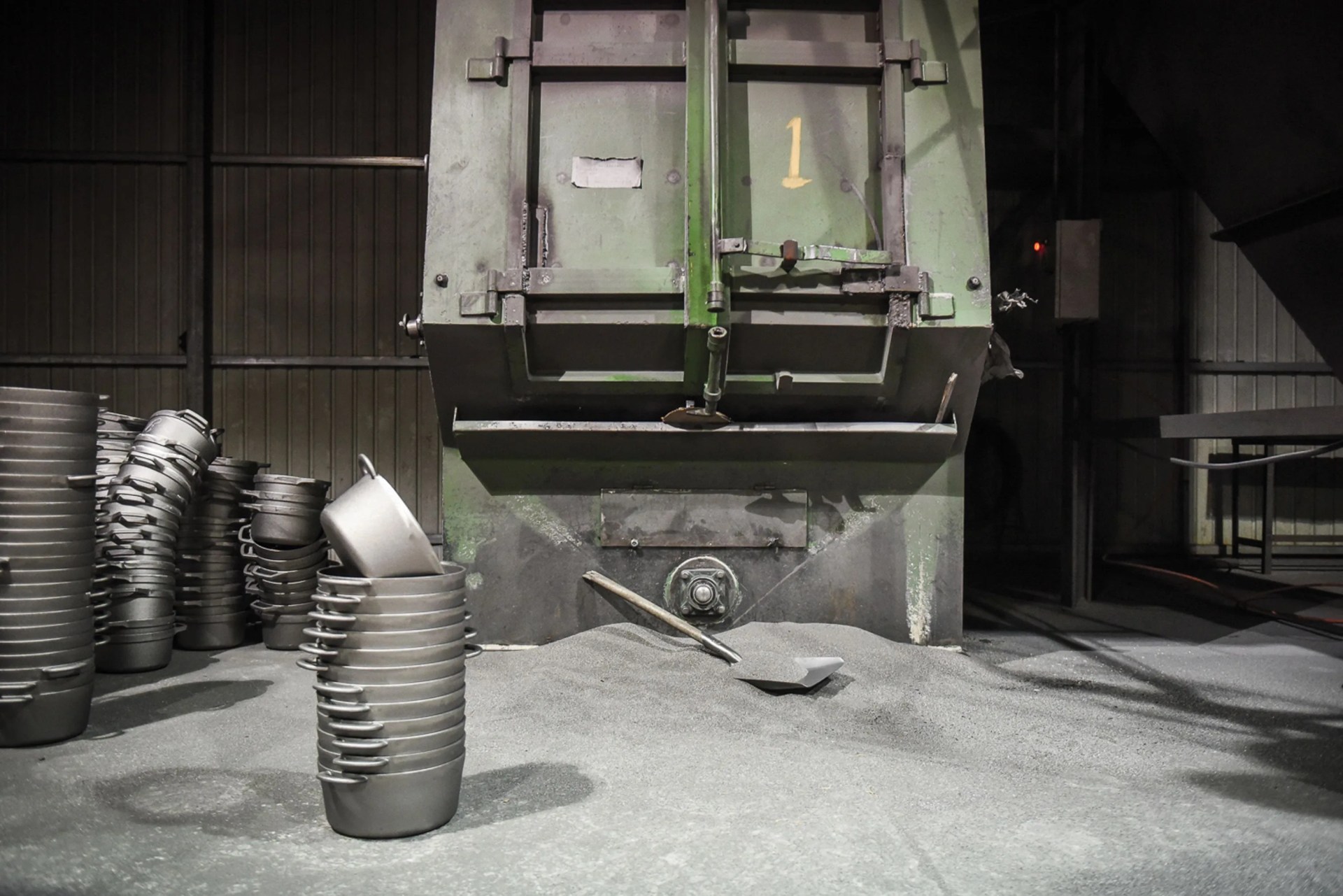 a large, greenish metal container with a pile of grain and a shovel in front of it