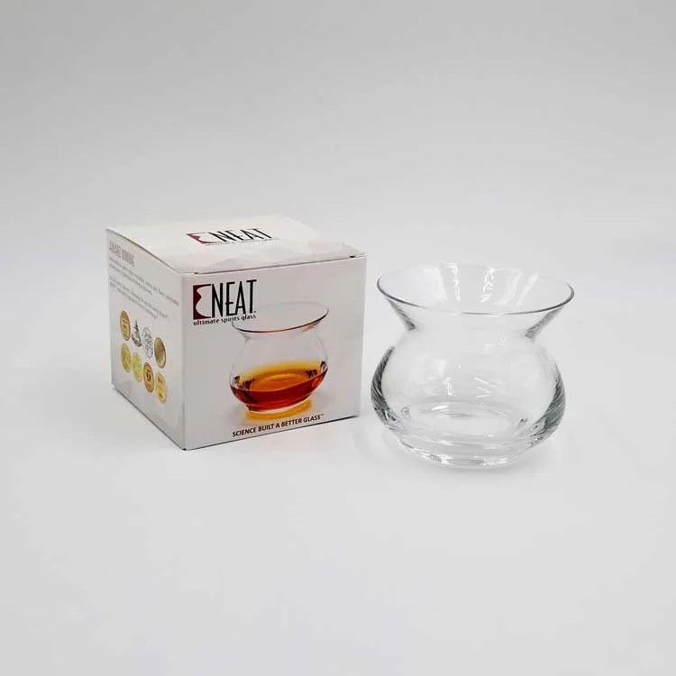 Artisan NEAT whiskey glass empty next to the glasses packaging on a grey backgroun
