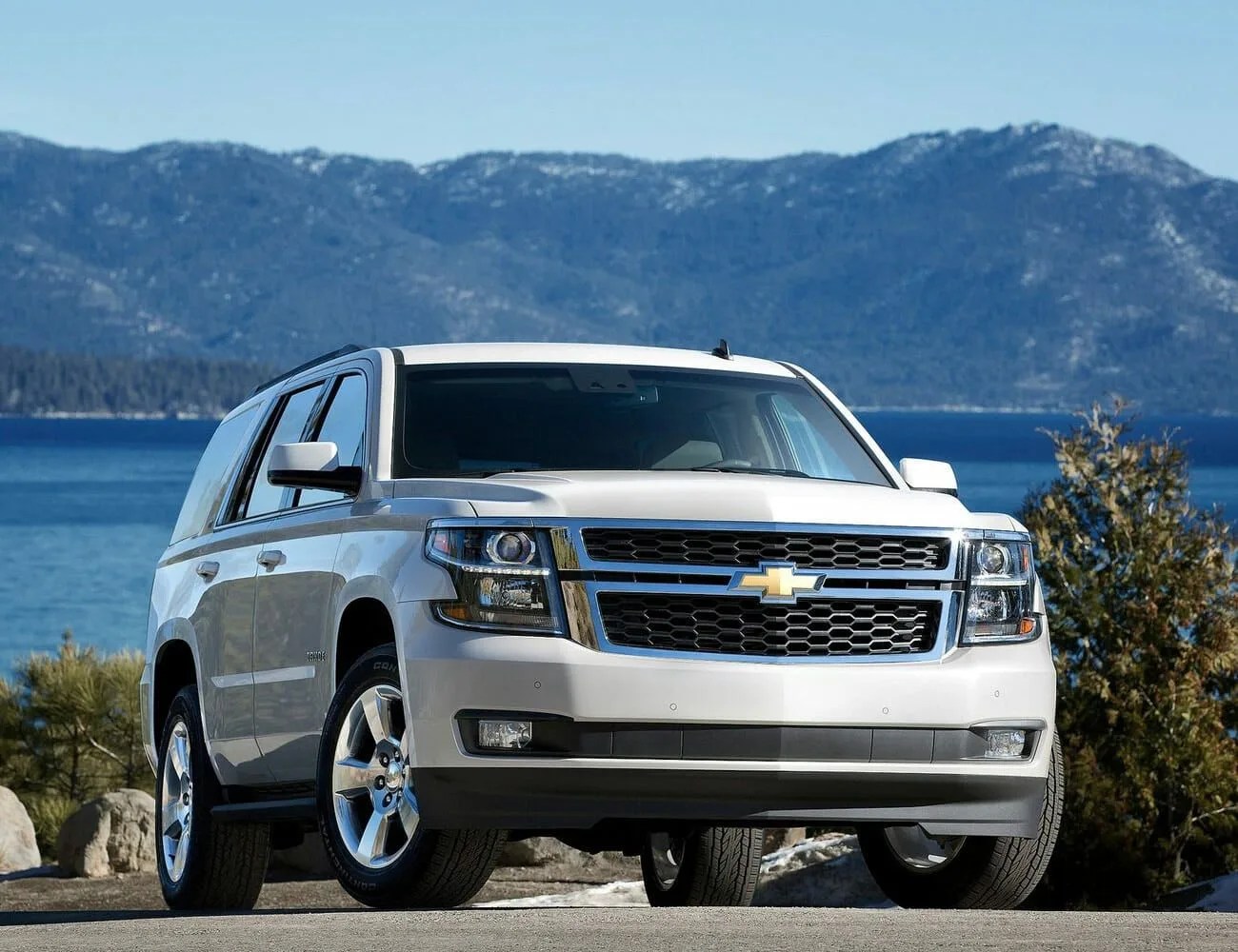 chevrolet tahoe parked in front of a lake with mountains in the background