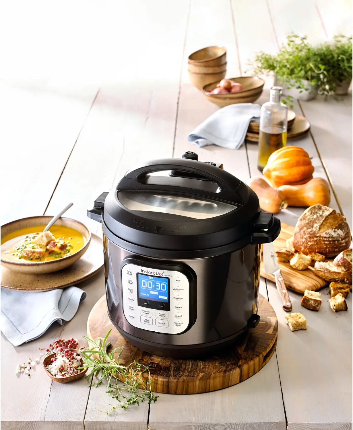 An Instant Pot Duo Nova on a table with various ingredients, vegetables , bread and soup.