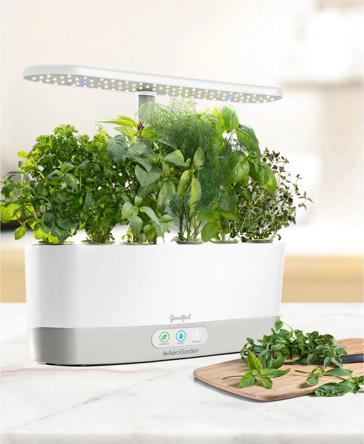 A countertop garden kit with herbs and herbs being cut on a wood cutting board with a knife.