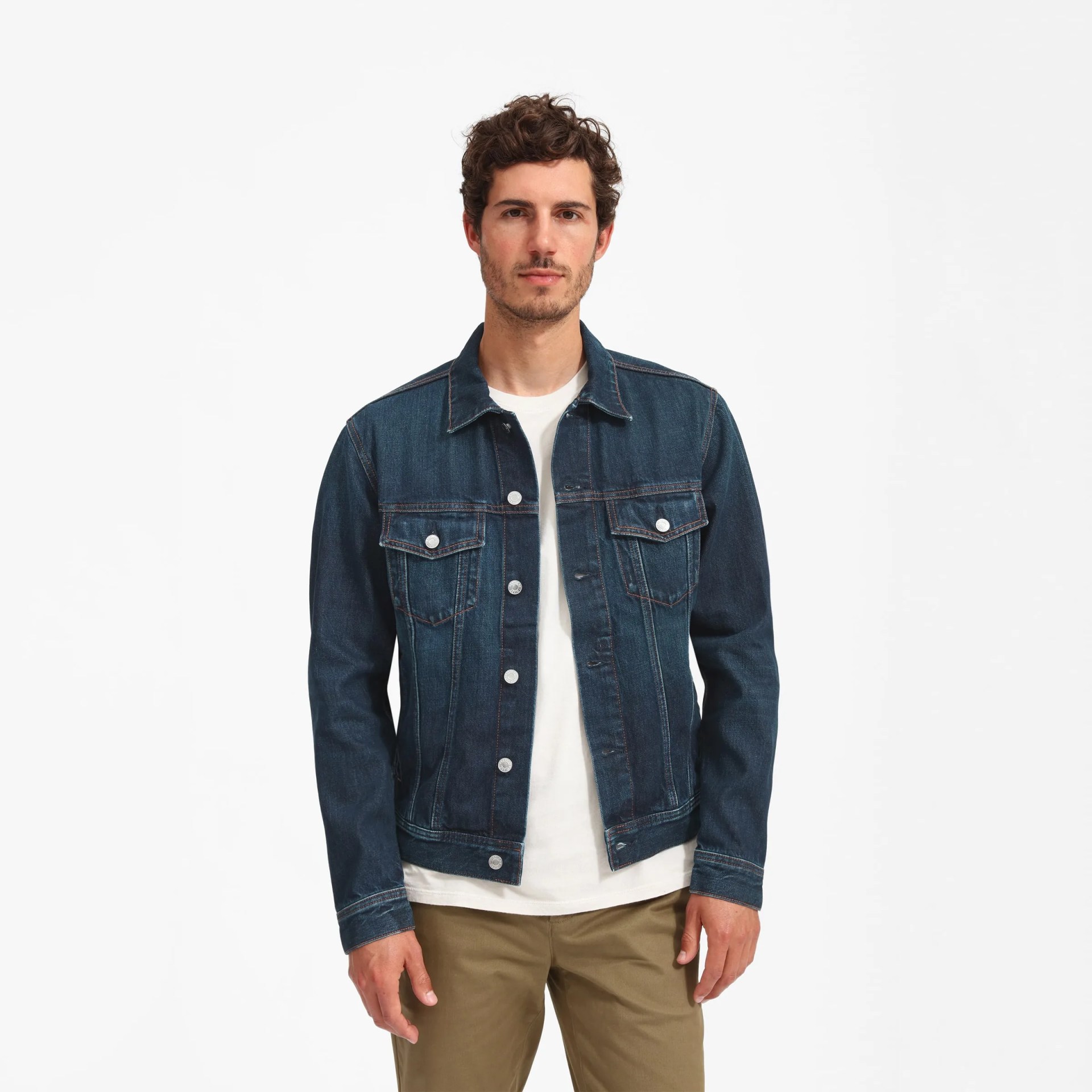 A dark blue denim jacket on a model with a white t-shirt and olive pants on a white background.