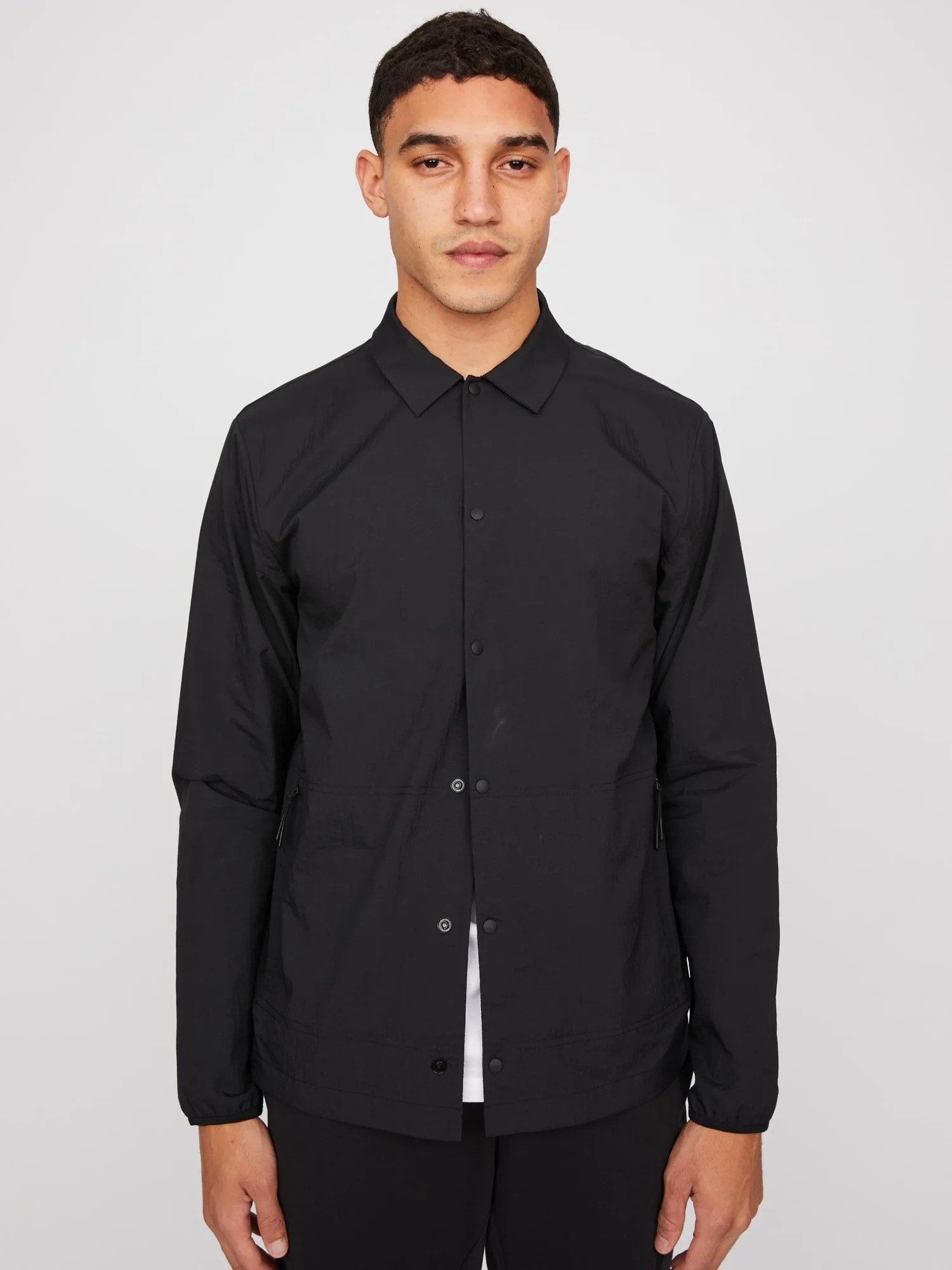 A black nylon button up jacket on a model on a white background.