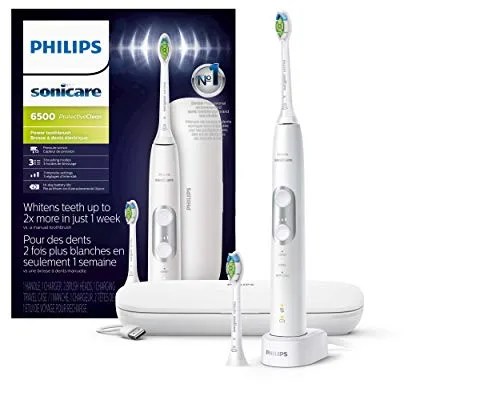 A white electric toothbrush with a product box, charging station and extra brush head all on a white background.