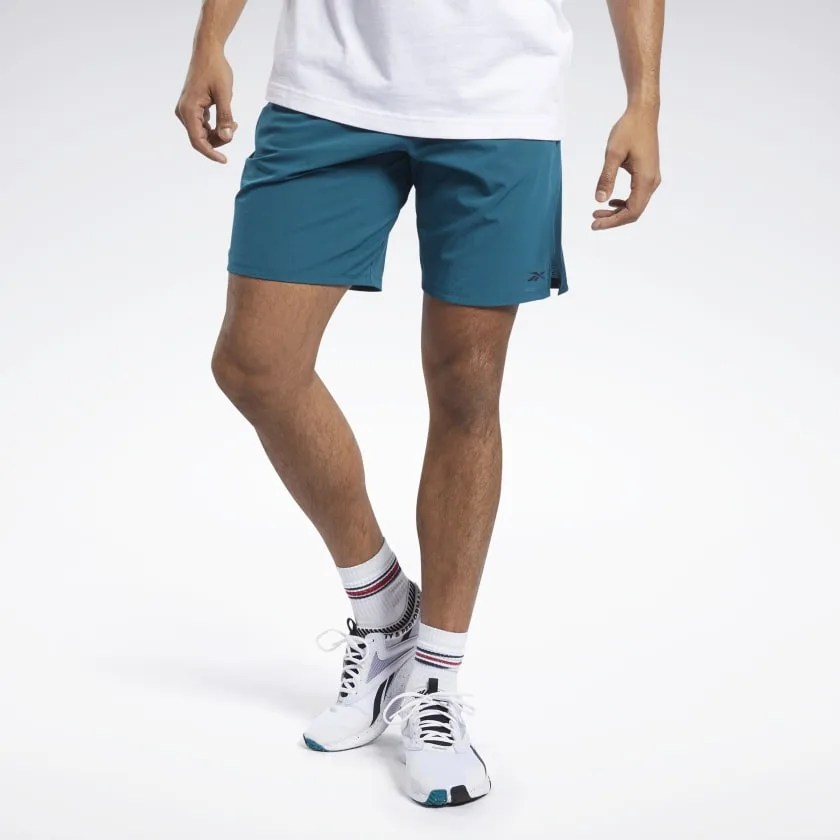 A model with teal shorts, a white shirt, white socks and sneakers on a white background.