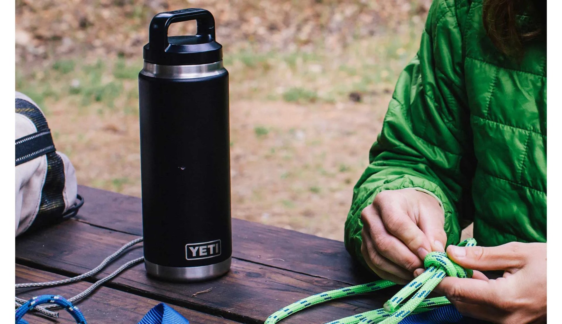 A black Yeti thermos with top on a picnic table with rope and a bag.