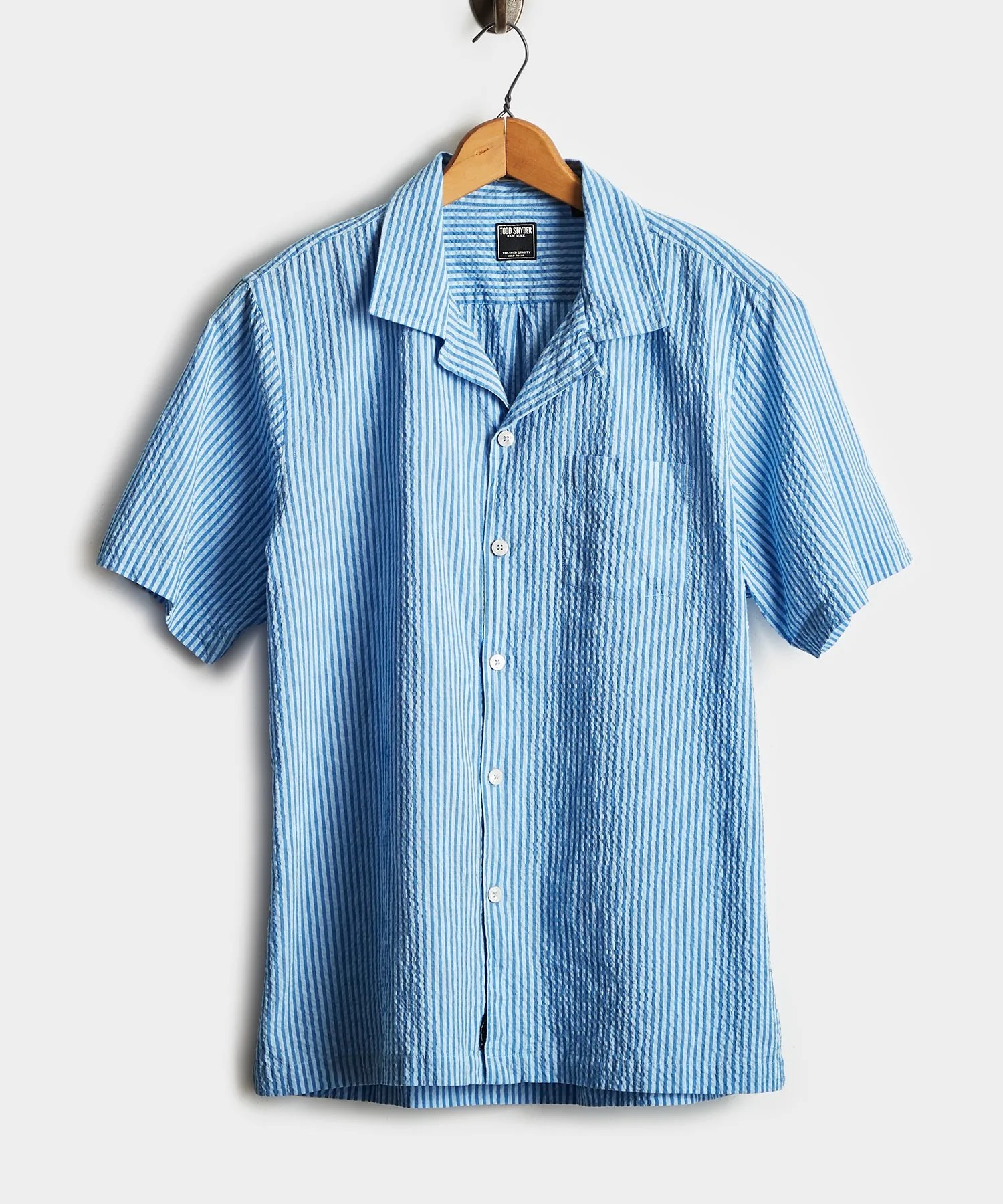 A light blue seersucker short sleeve button down shirt on a hanger on a gray background.