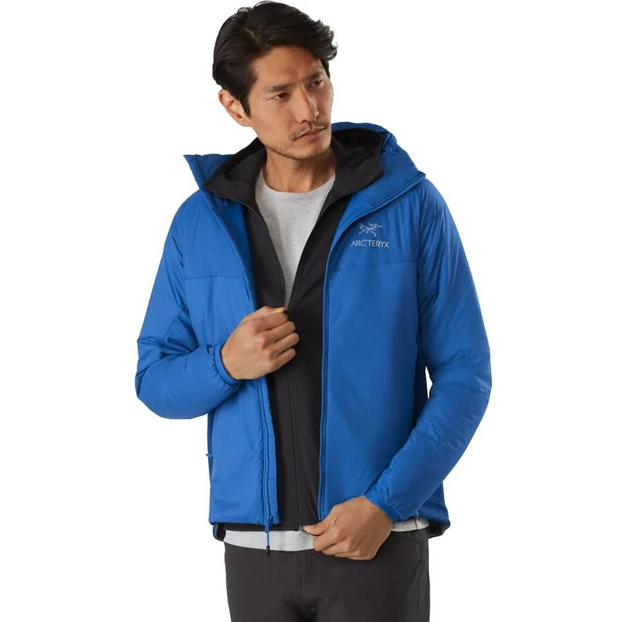 a man with black hair wearing an unzipped blue insulated jacket