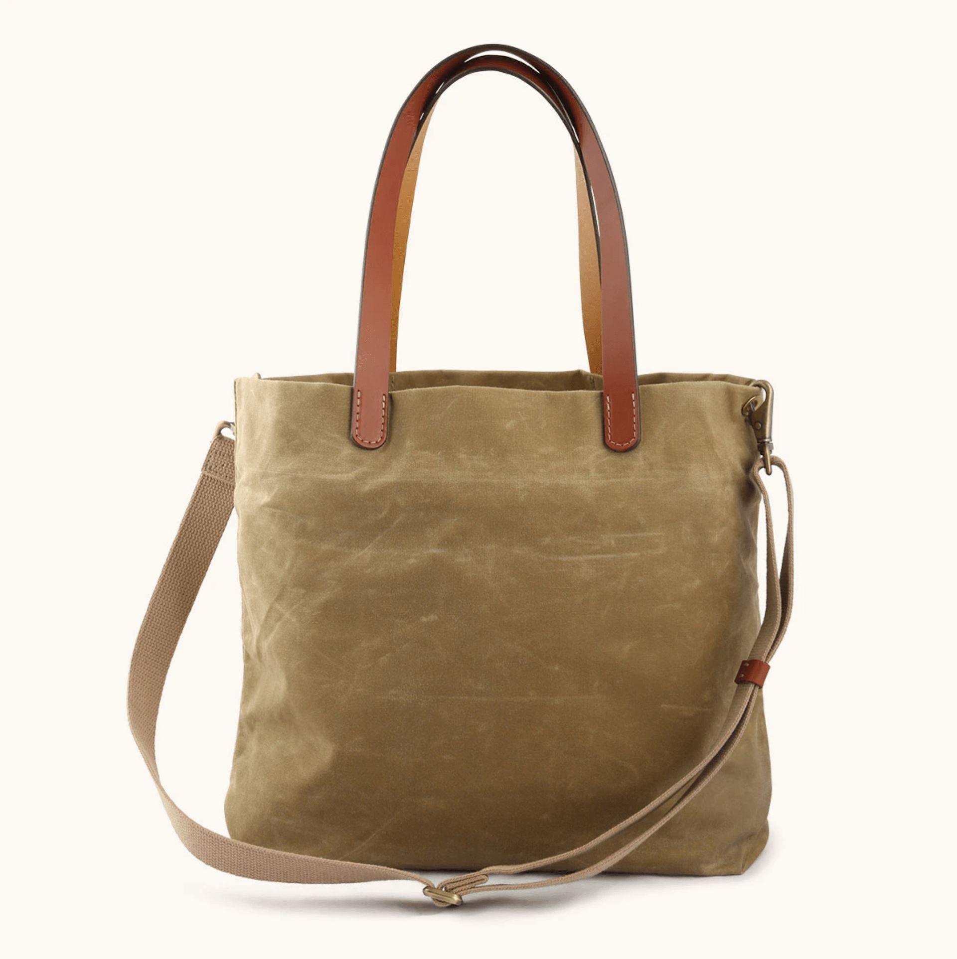 A tan waxed canvas tote with a shoulder strap and handles on a white background.
