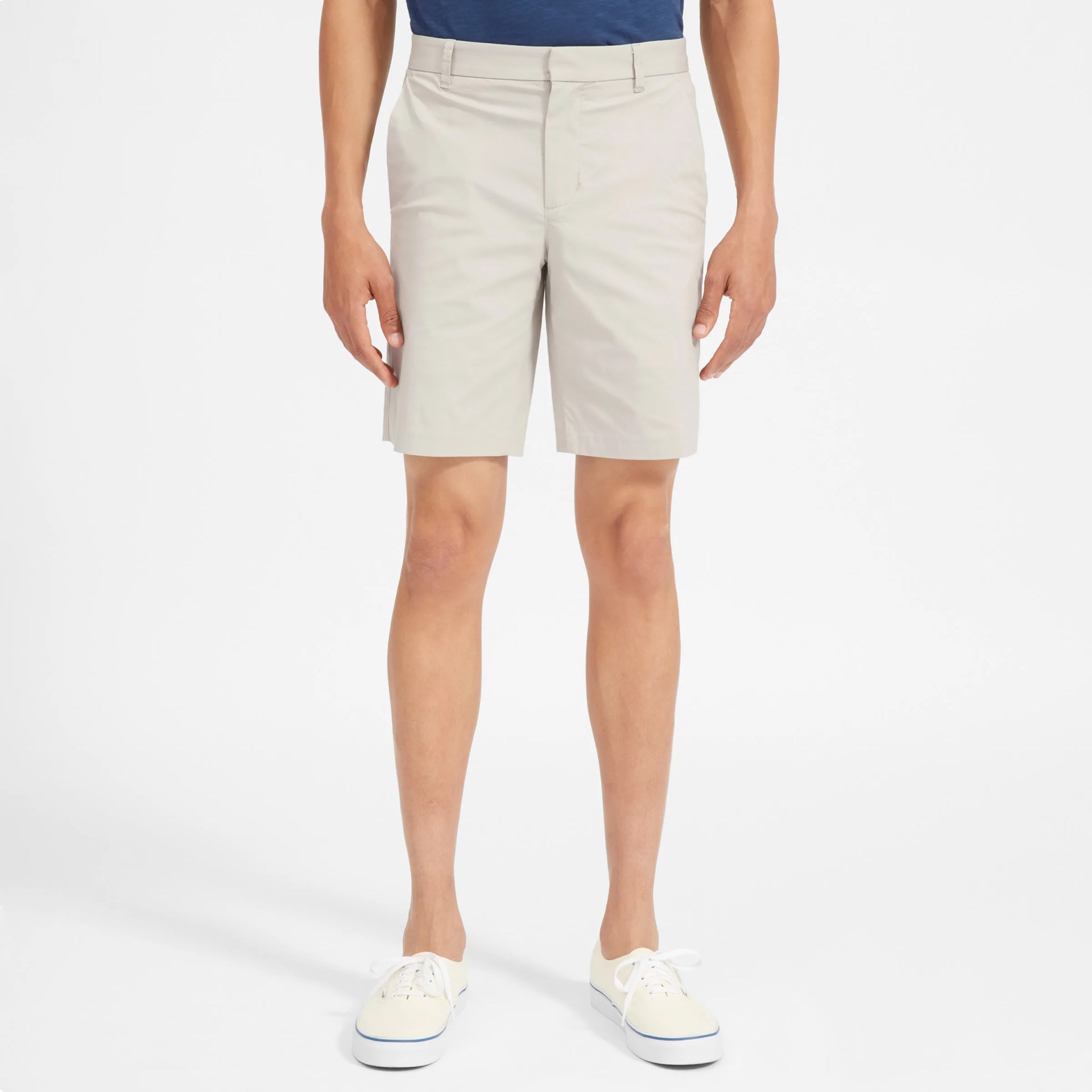 A model with khaki shorts, a blue shirt and white shoes on a gray background.
