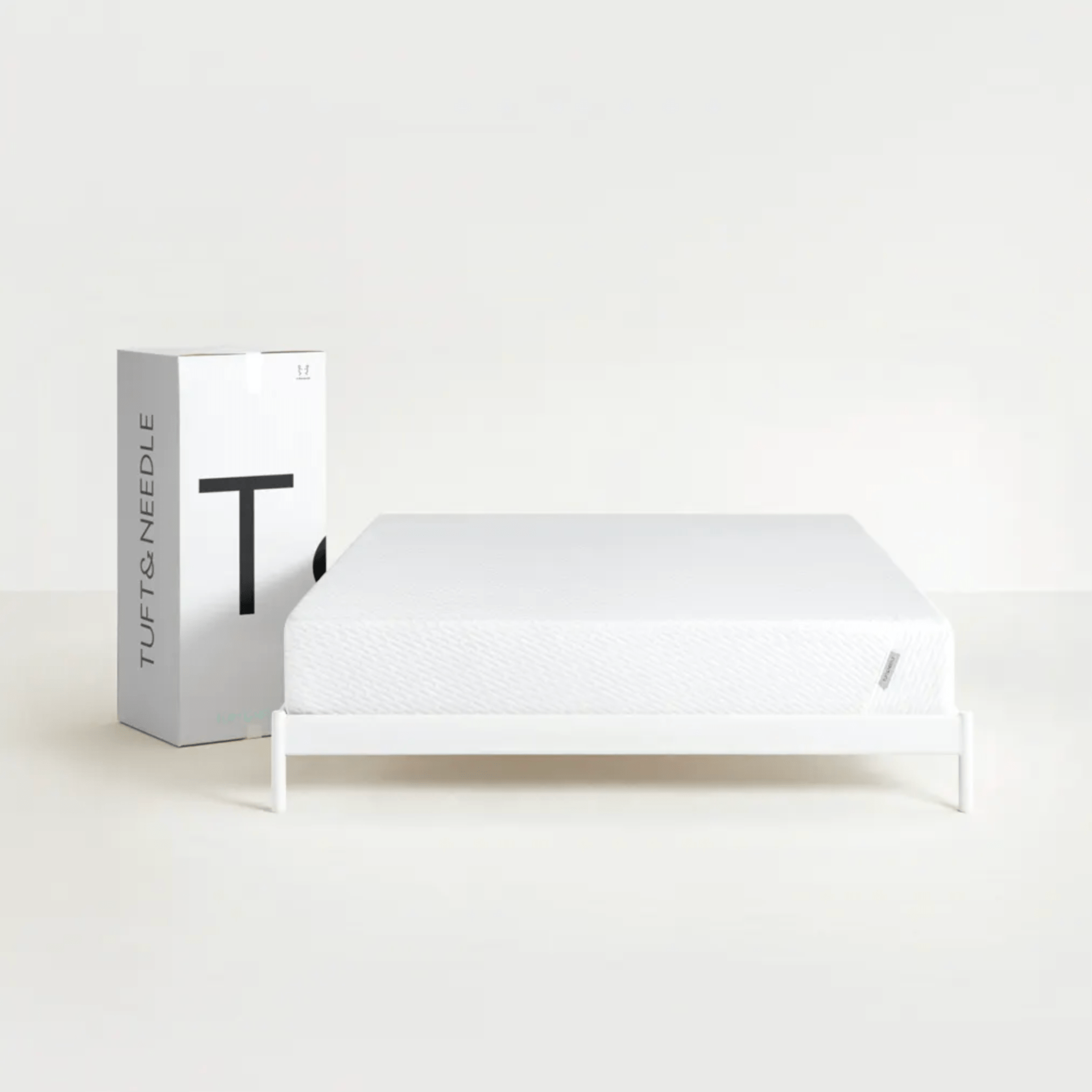 A white mattress on a white platform bed with a white cardboard box.