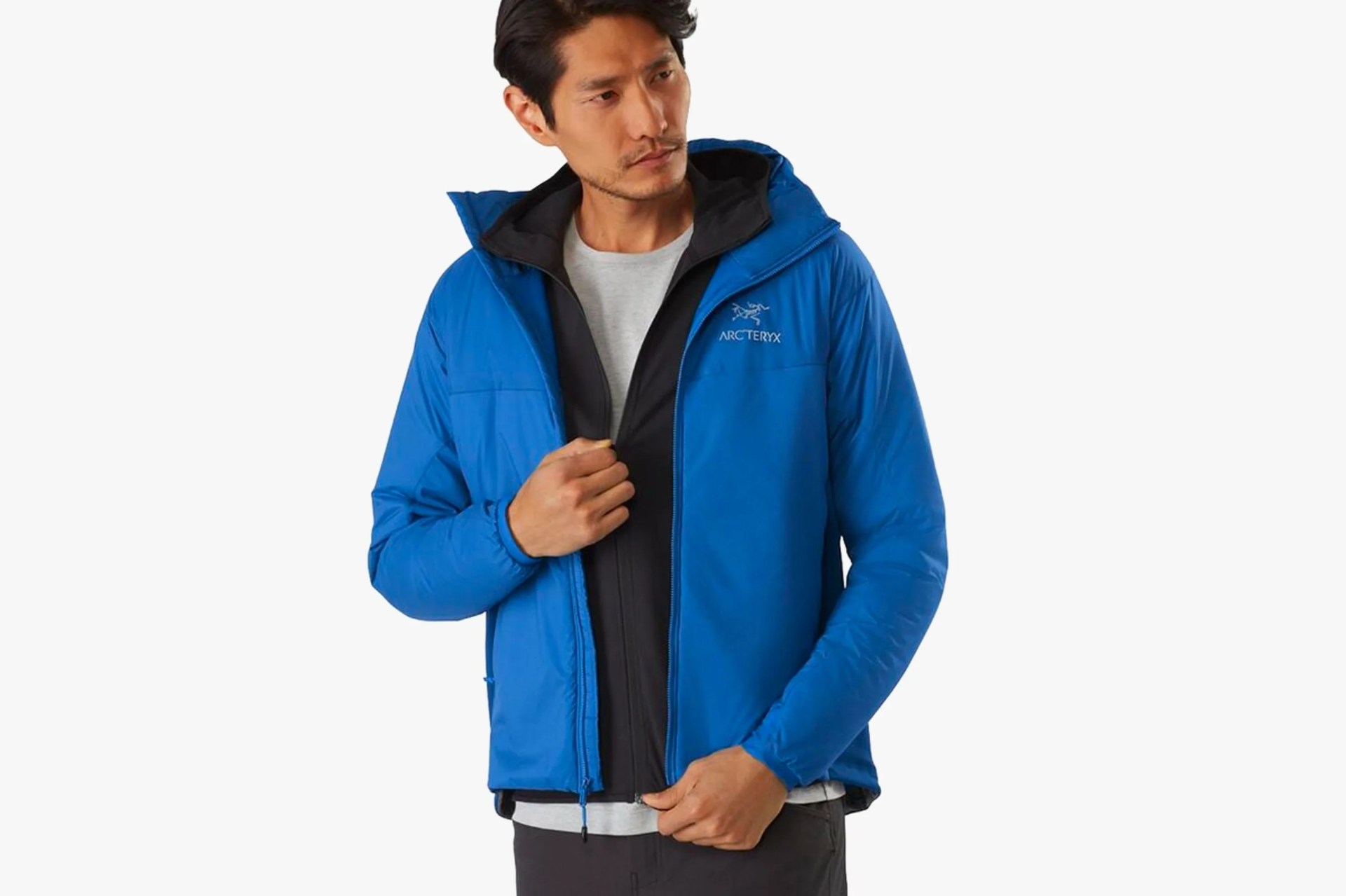 a man with black hair wearing an unzipped blue insulated jacket