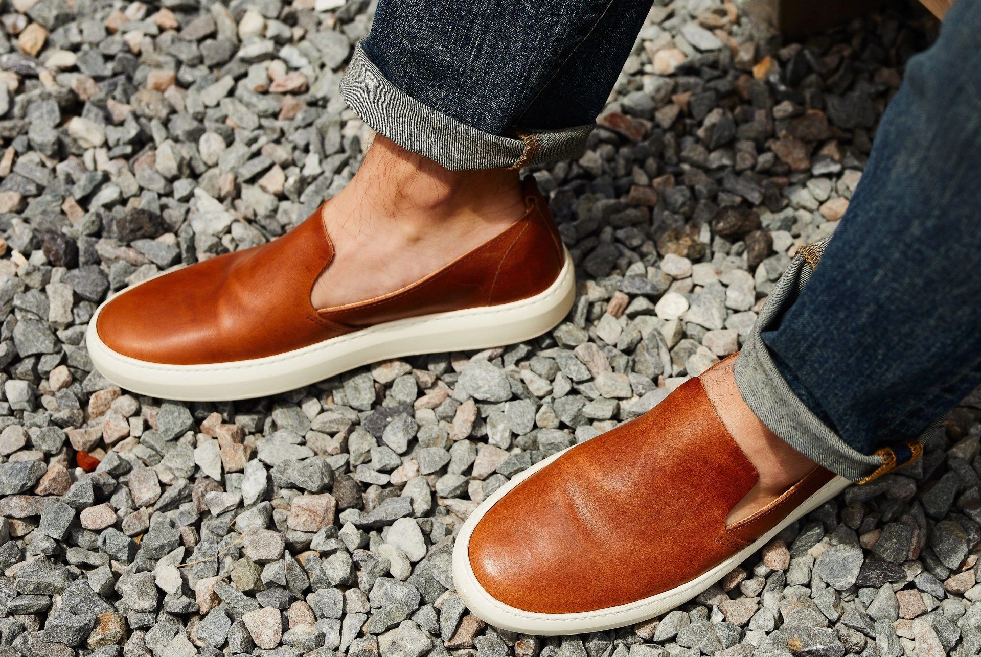 brown sneakers and blue jeans on model against gravel background