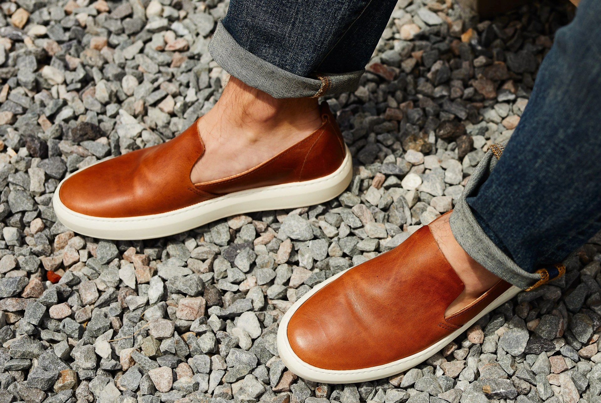 brown sneakers and blue jeans on model against gravel background
