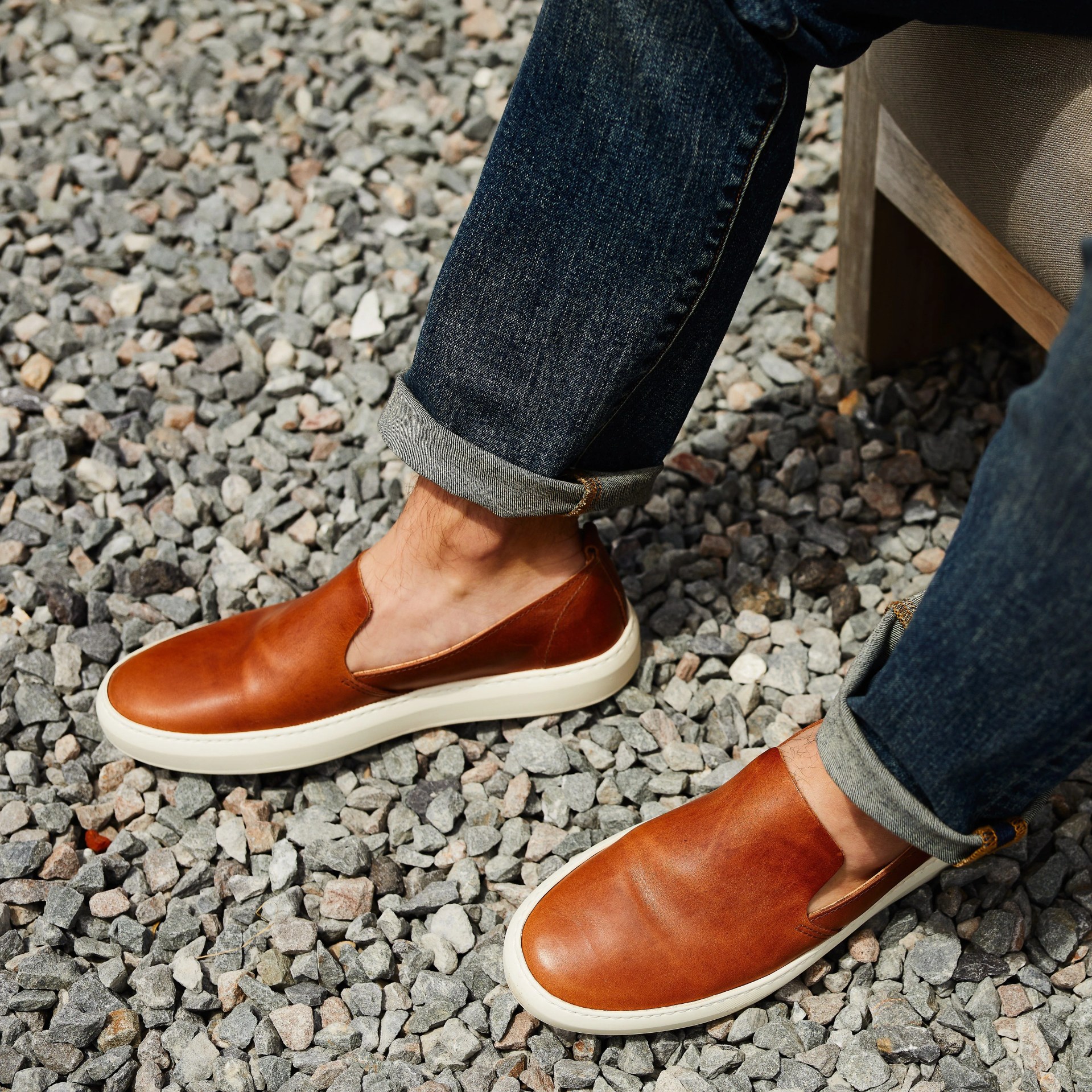 brown sneakers and blue jeans on model against gravel background