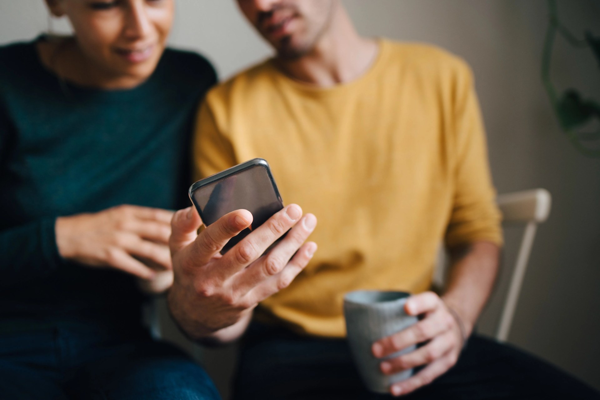 midsection of boyfriend showing smart phone to girlfriend while having coffee at home