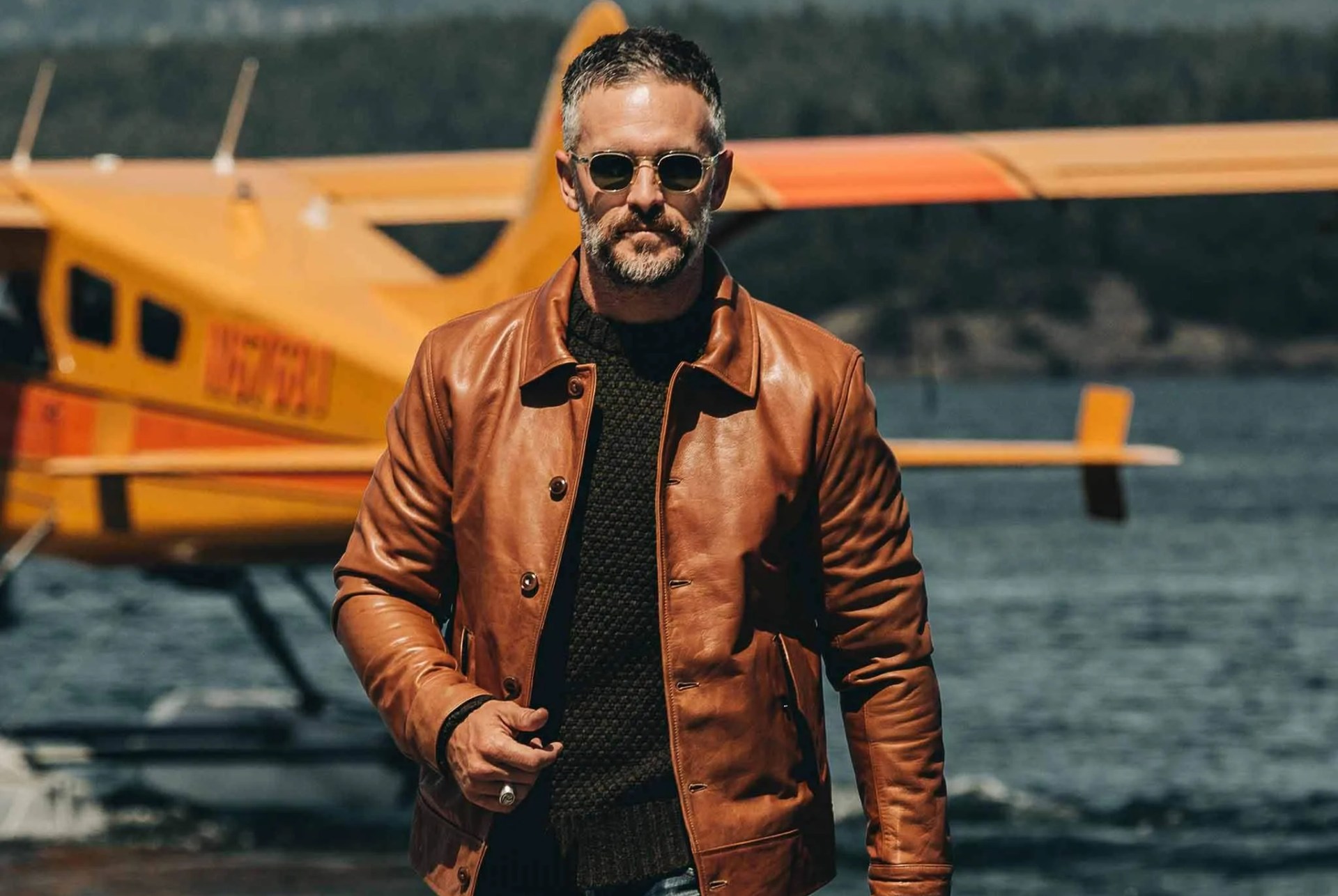 ma wearing leather jacket in front of a lake with a waterplane