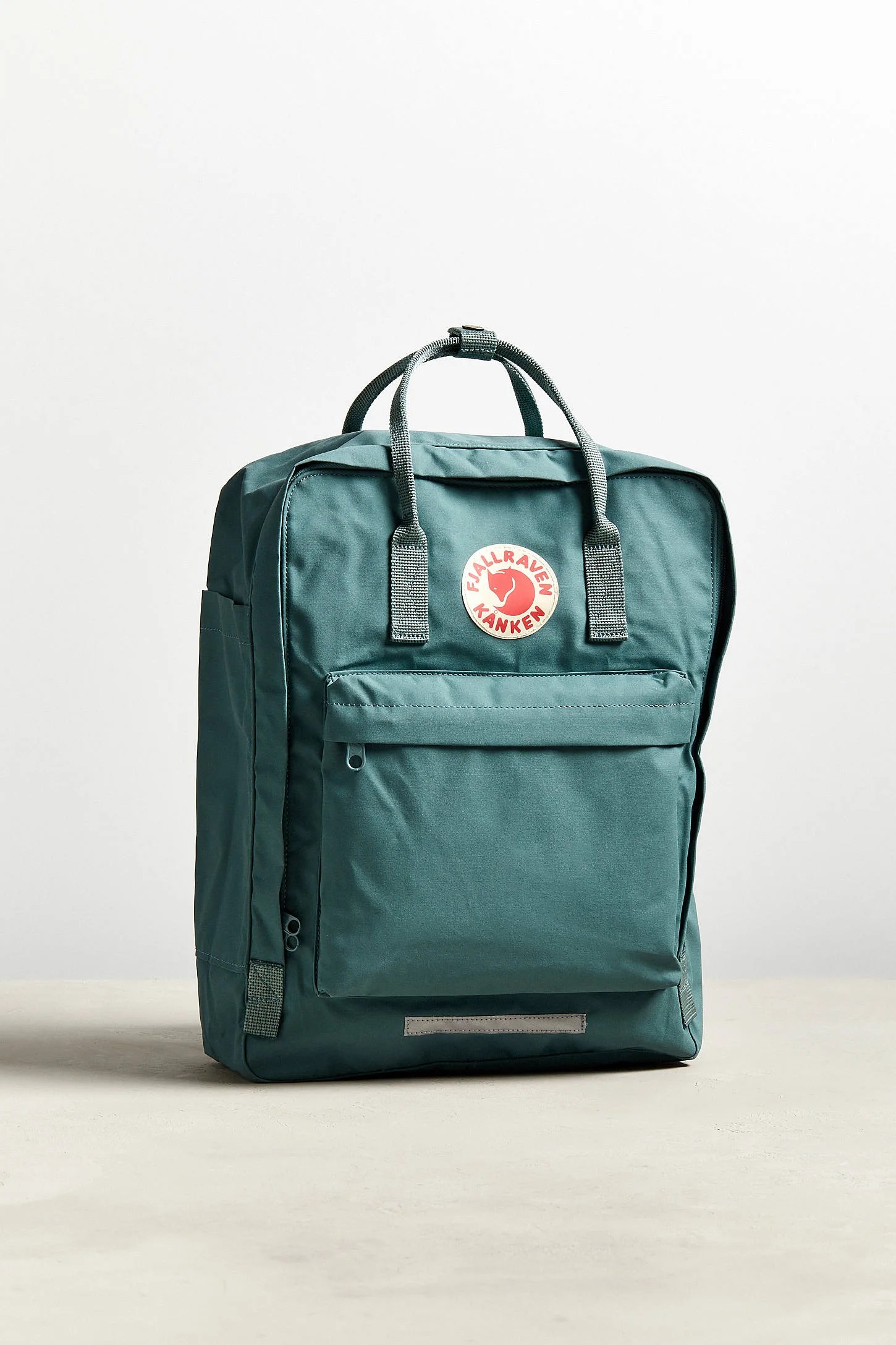 A mint colored backpack with handles on a gray background.