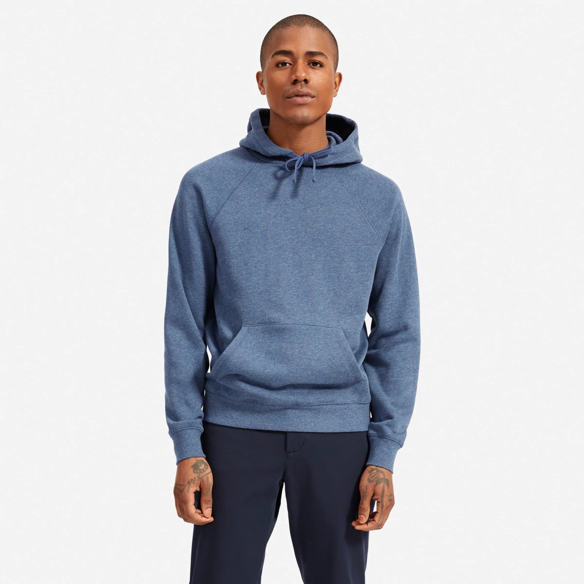 A model wearing a blue hoodie sweatshirt and blue slacks on a gray background.
