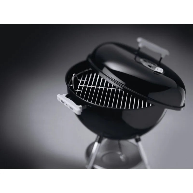 a black charcoal grill and lid on a gray background