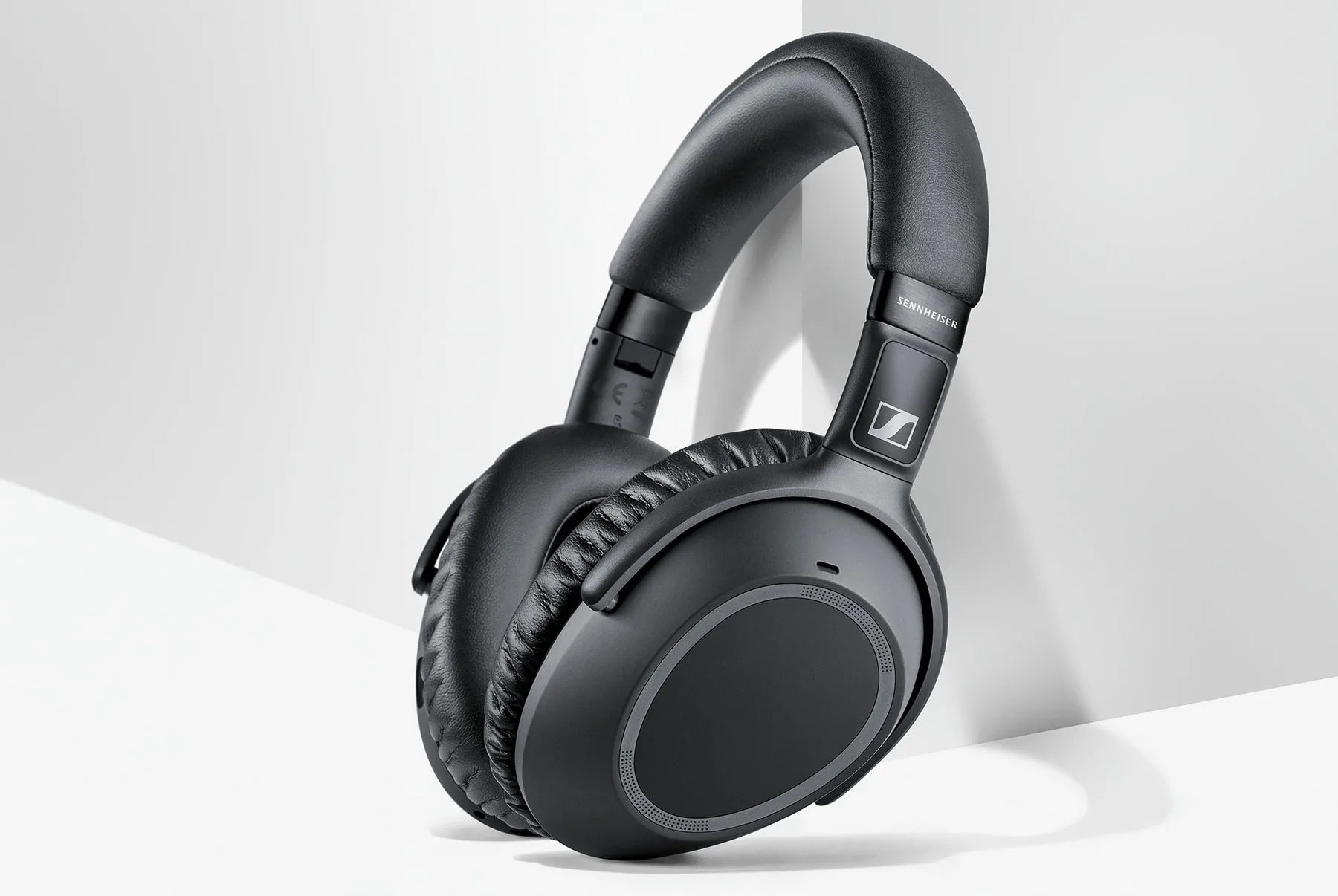 A pair of black wireless over-ear headphones leaning up against a wall.