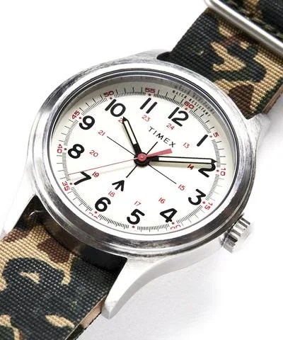 A field watch with an olive and camo canvas strap on a gray background.