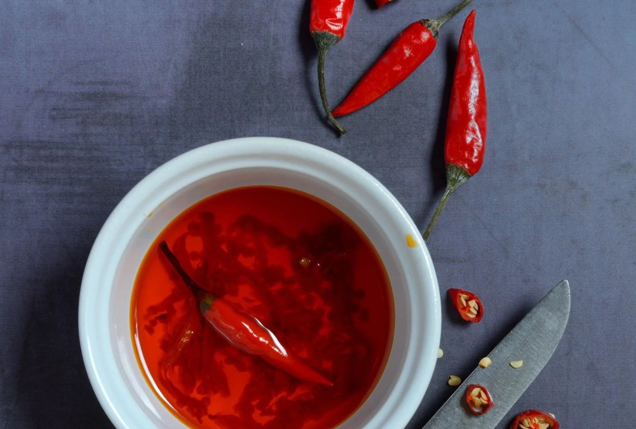 chili oil in bowl with knife and chili peppers, food photography, studio shot, germany