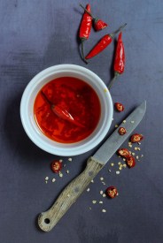 chili oil in bowl with knife and chili peppers, food photography, studio shot, germany