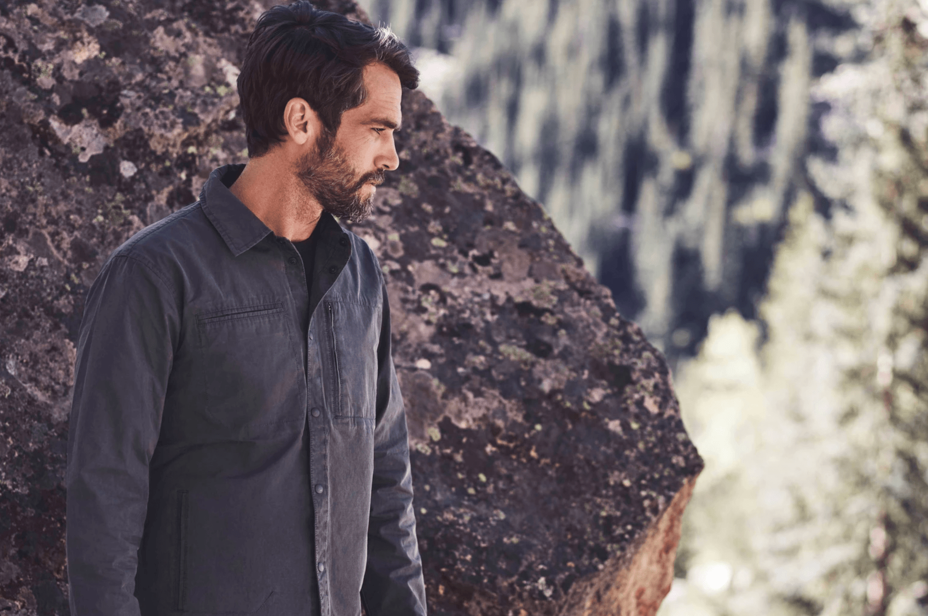 a model in front of a boulder wearing a graphite jacket