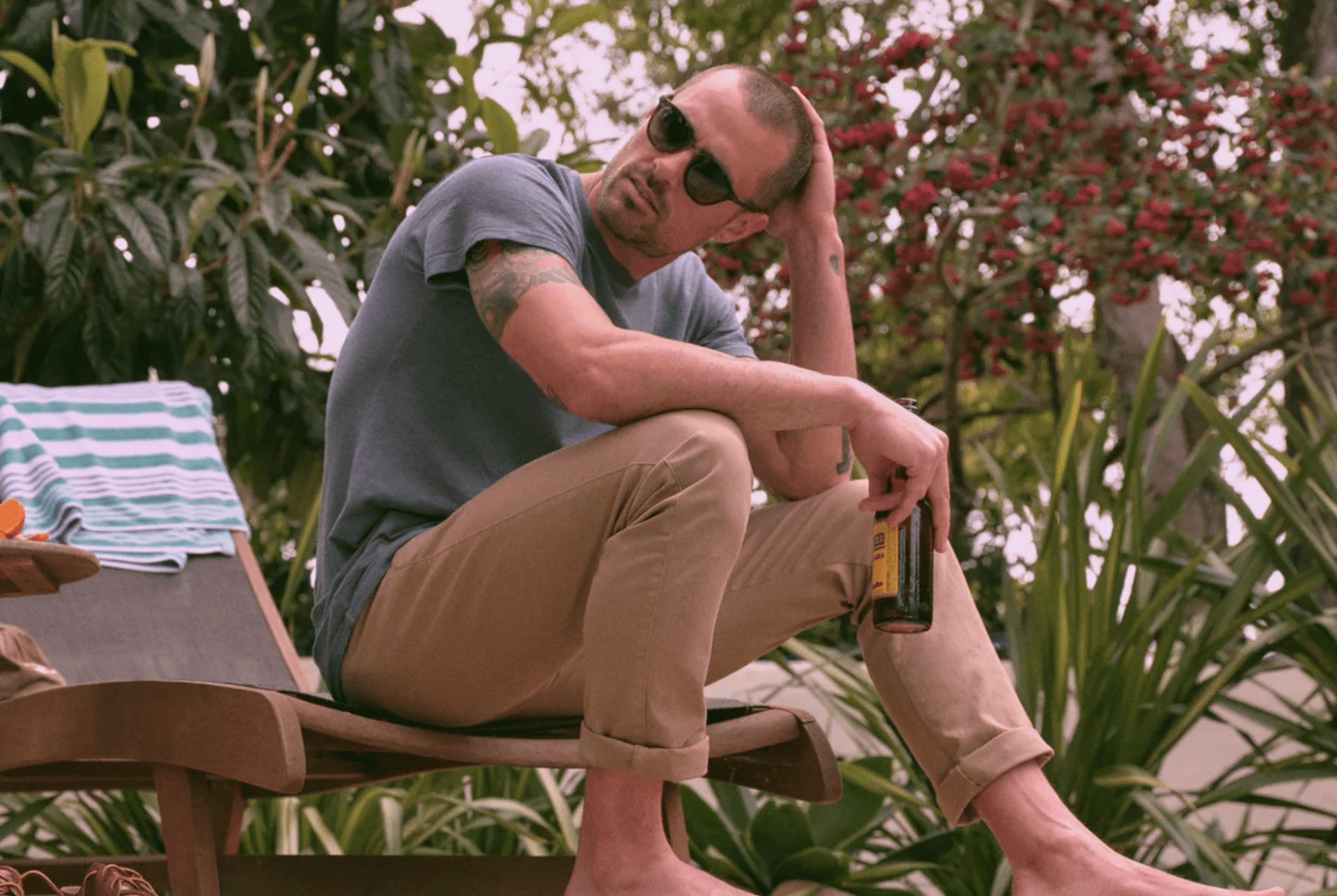 a model sitting by a pool with a beer, khakis and a gray t shirt