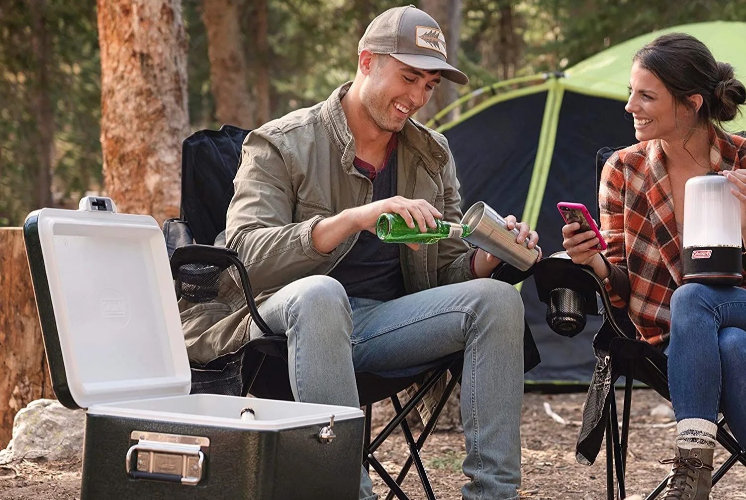 a campsite with a cooler, logs, a couple in camping chairs and a tent