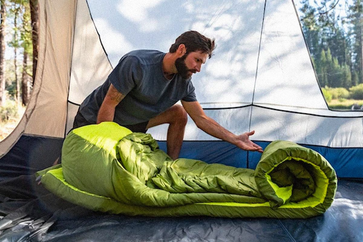 a man unrolling a green sleeping bag and camping mattress