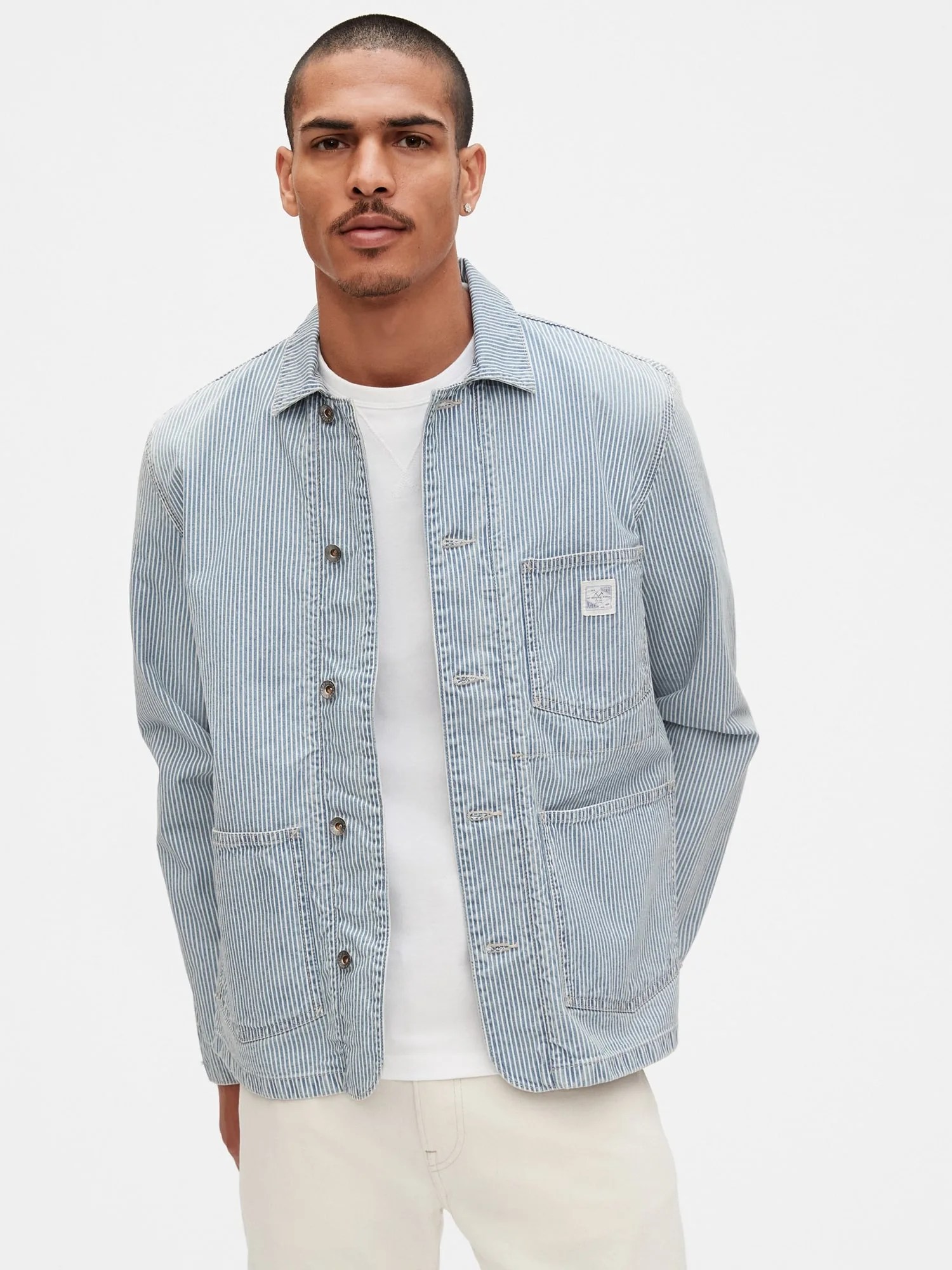 A model wearing a railroad stripe blue chore coat and white t-shirt on a gray background.