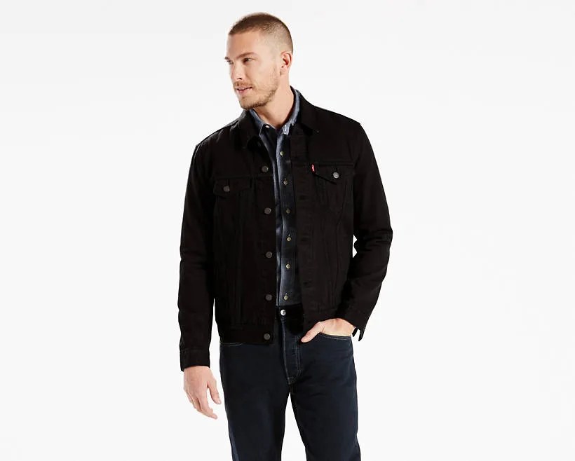 A model wearing a black denim jacket and black jeans on a gray background.