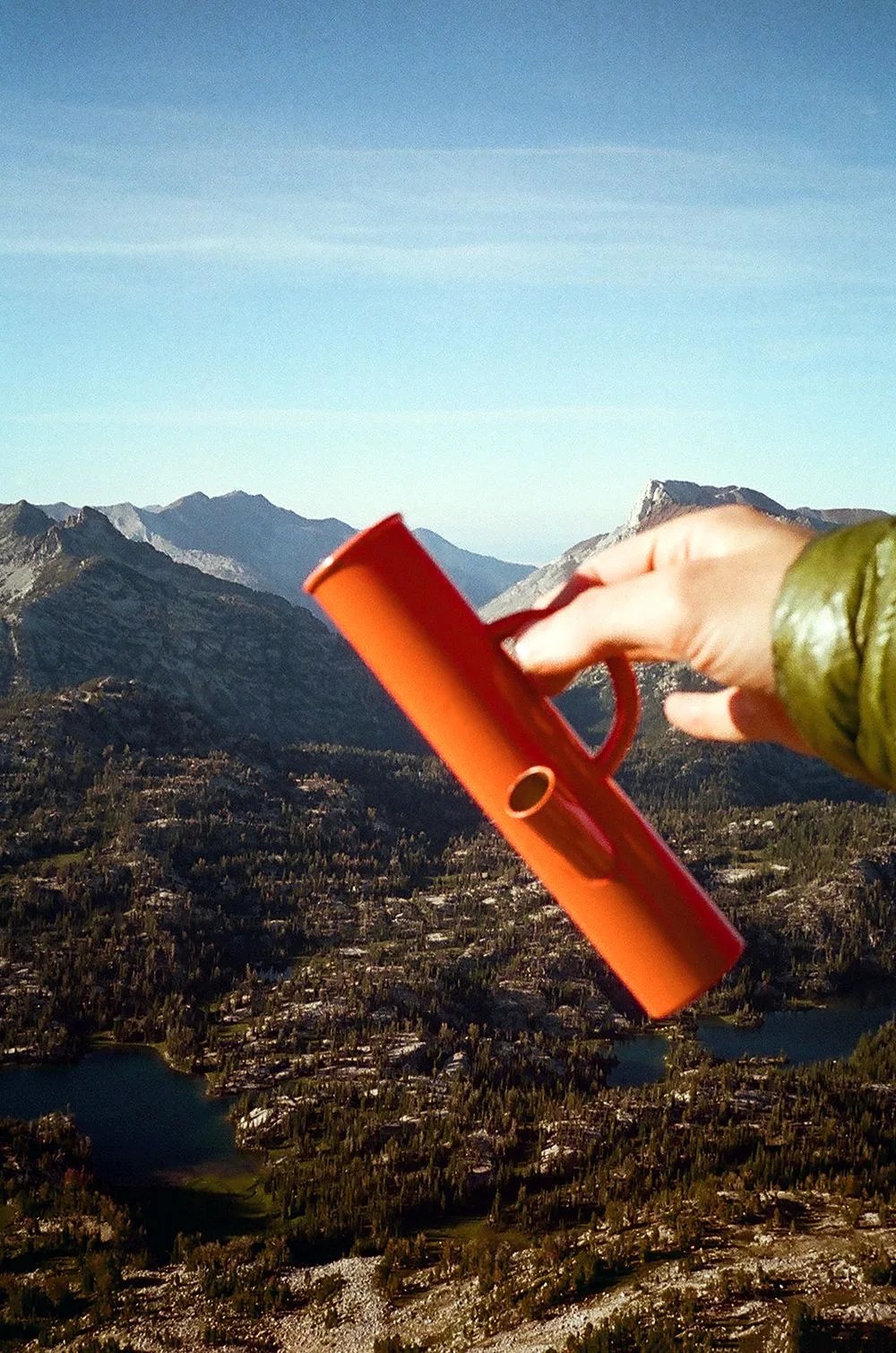a hand holding an orange bong against a mountain backdrop