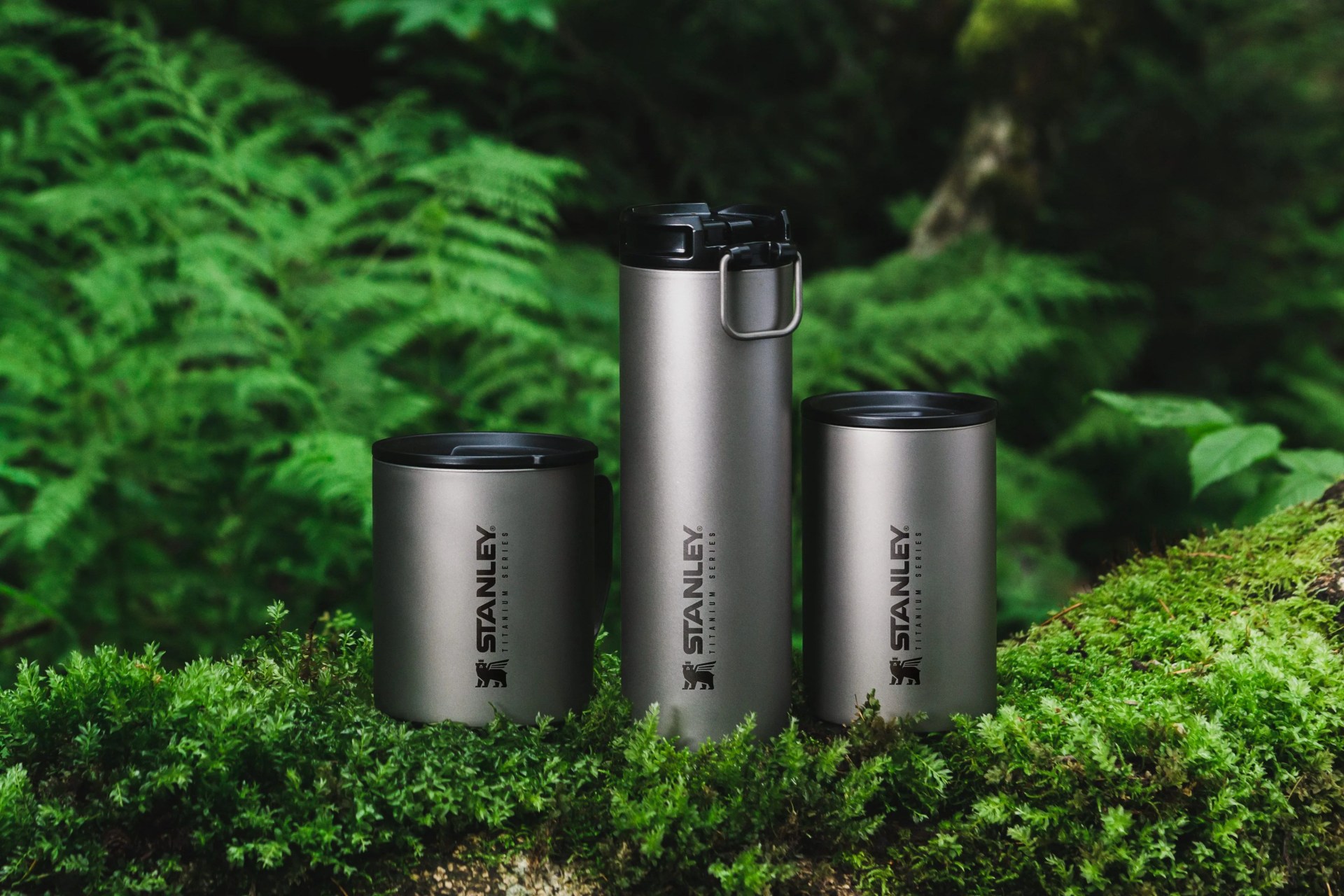 three titanium mugs of different heights near plants