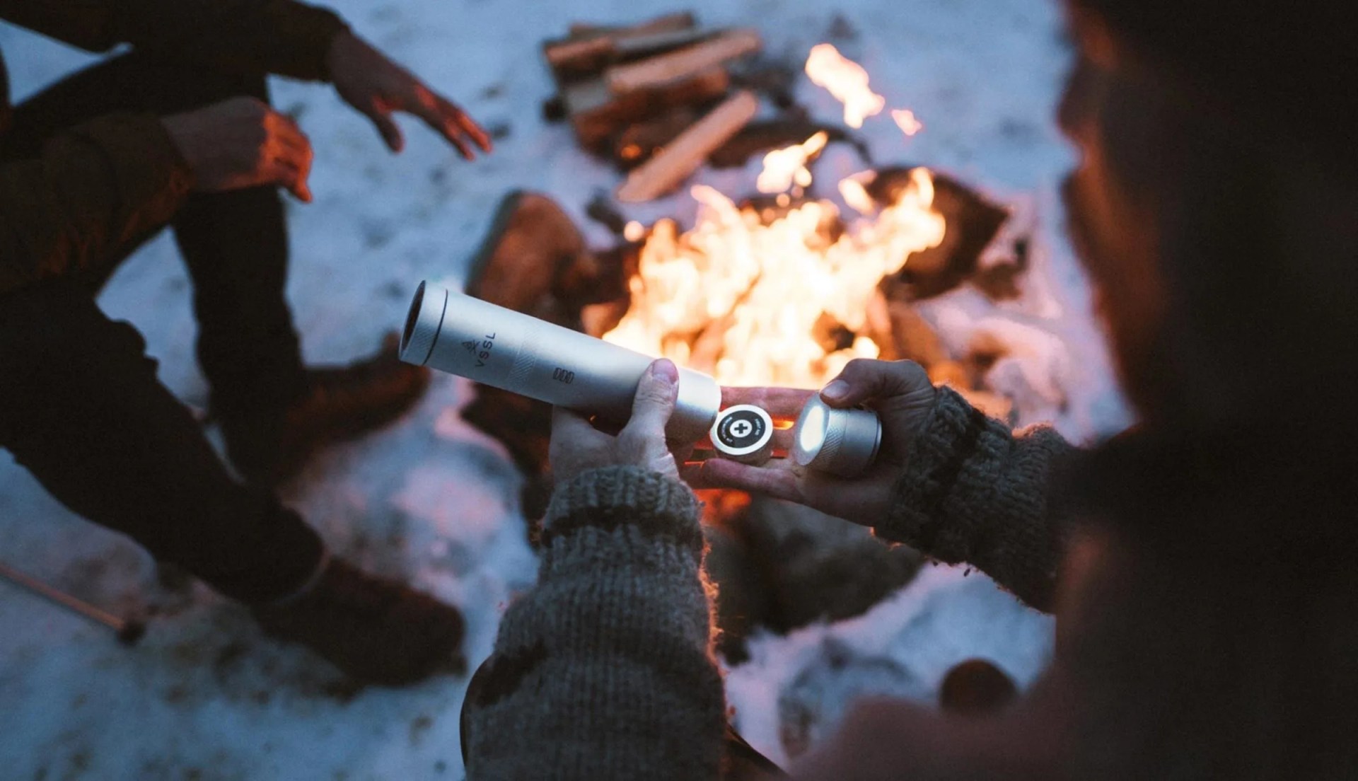a man opening a metal cylinder near a campfire