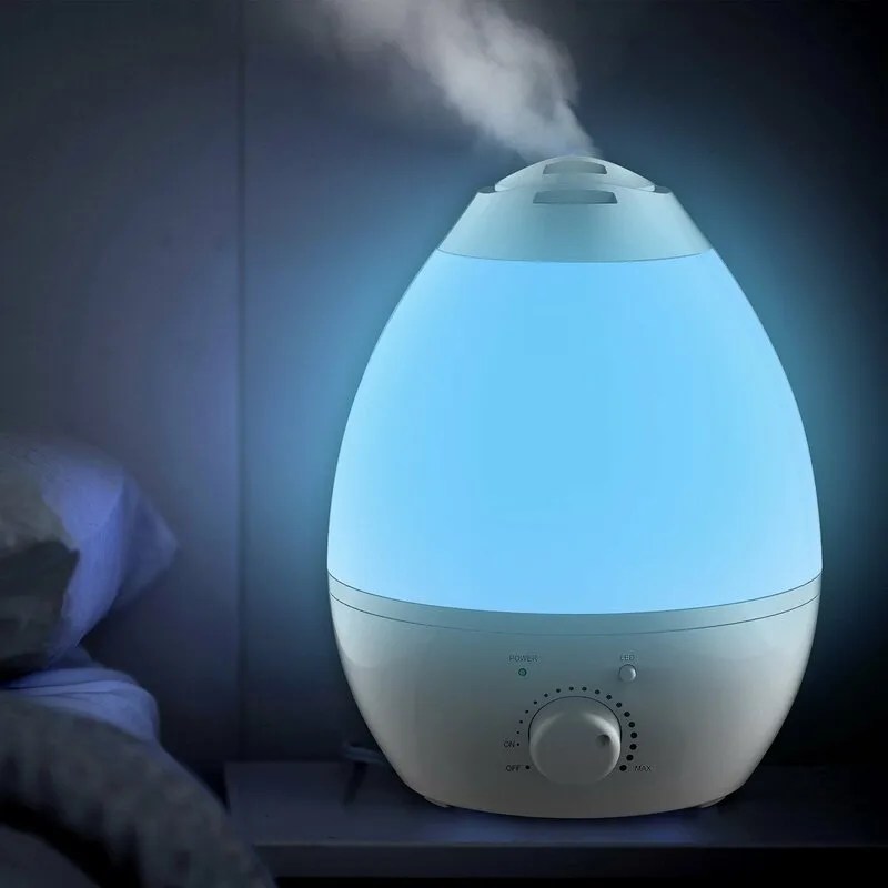 A humidifer on a nightstand next to a bed