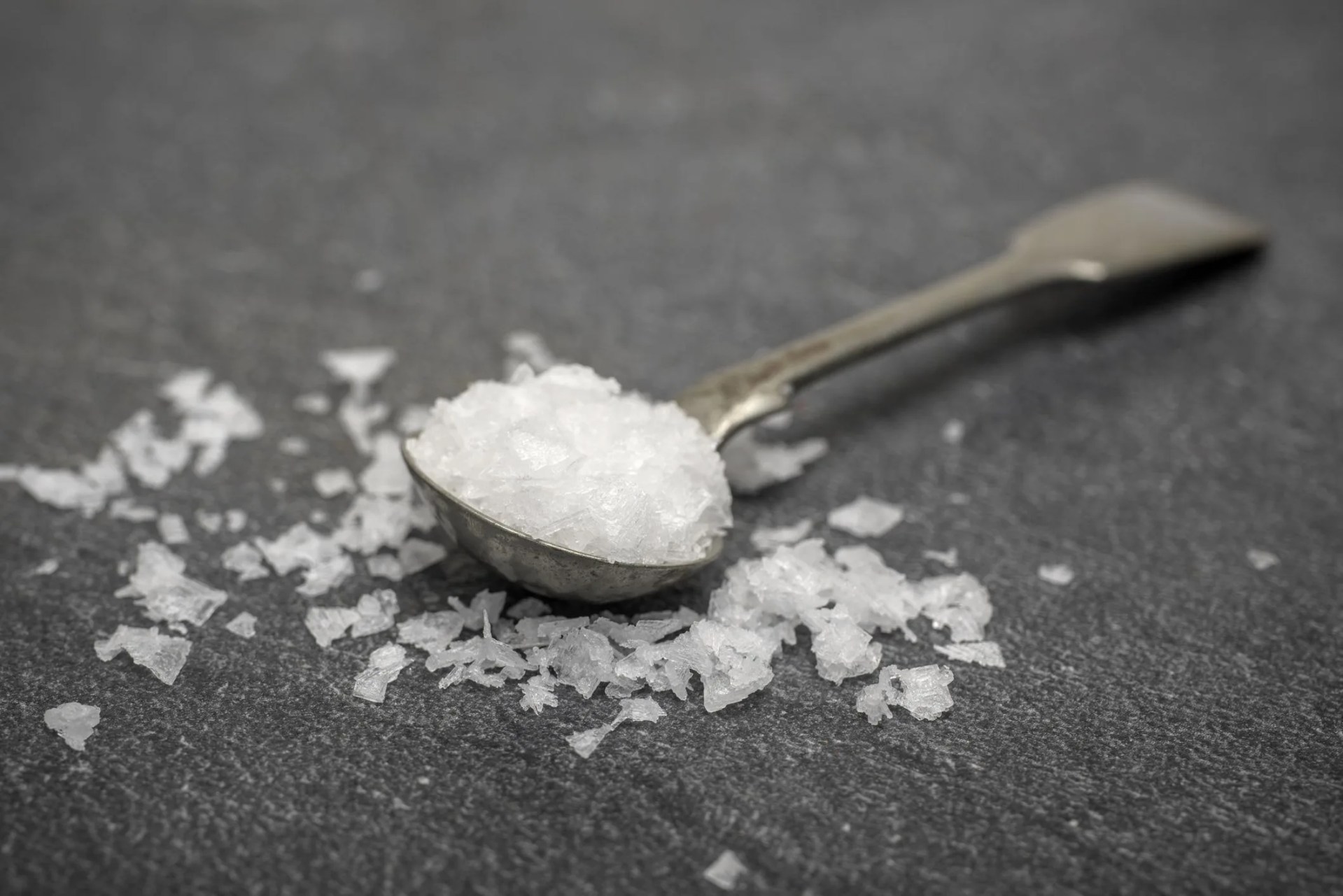 a spoon full of sea salt crystals on a stone background