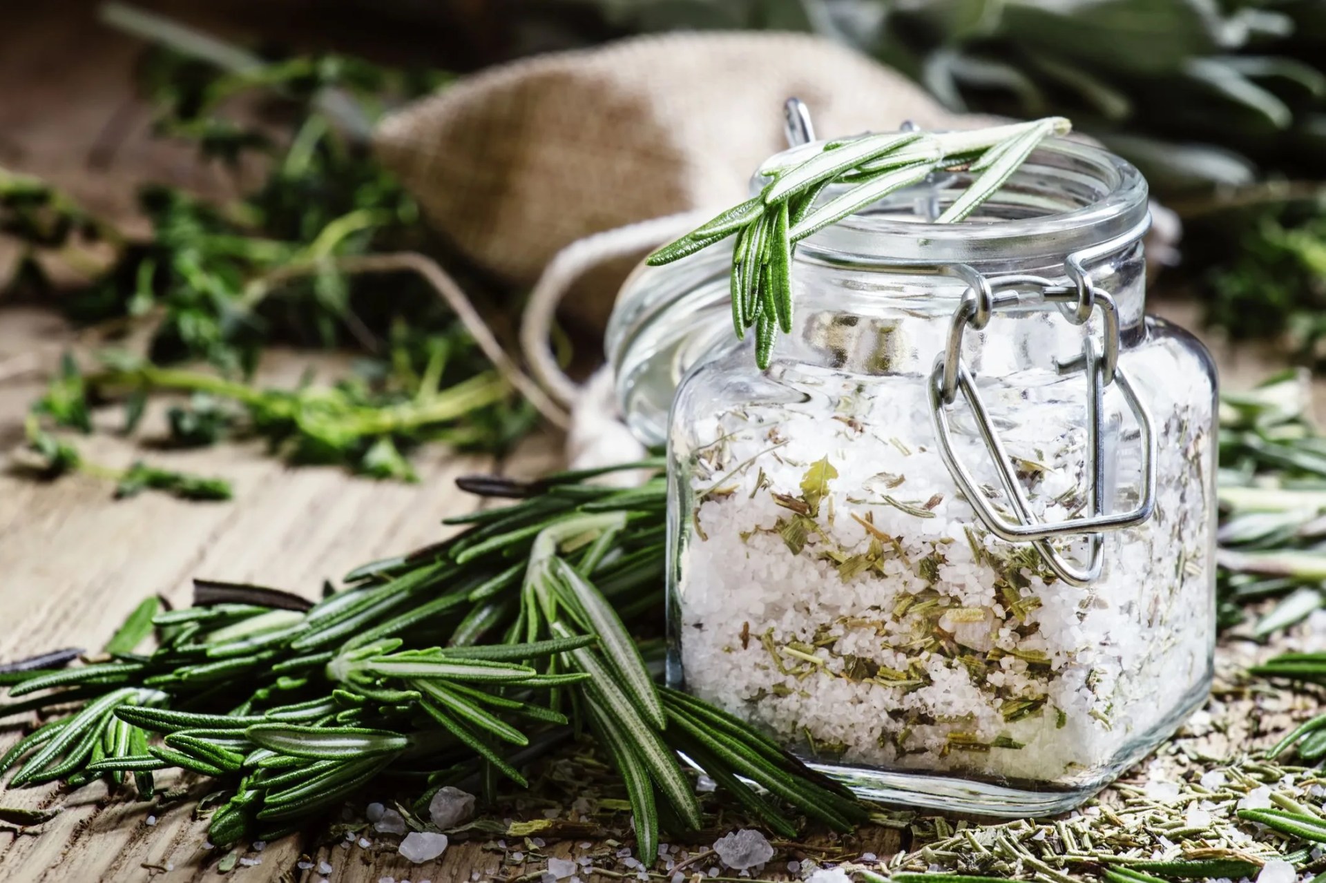 sea salt with dried rosemary in a glass jar, vintage wooden background, selective focus