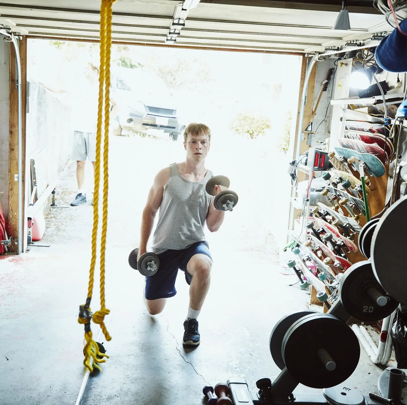 young man doing lunges with dumbbells in gym in garage