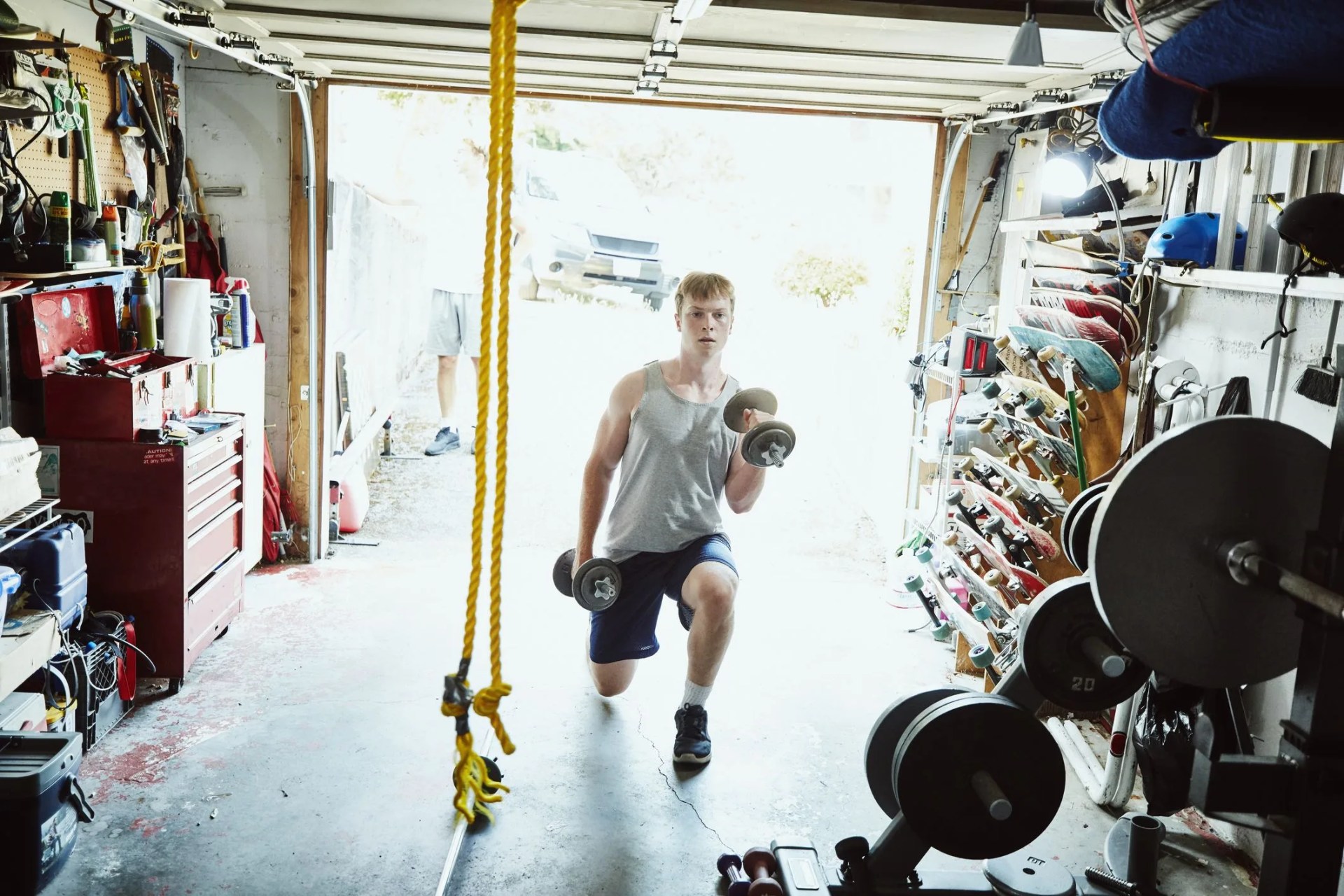 young man doing lunges with dumbbells in gym in garage