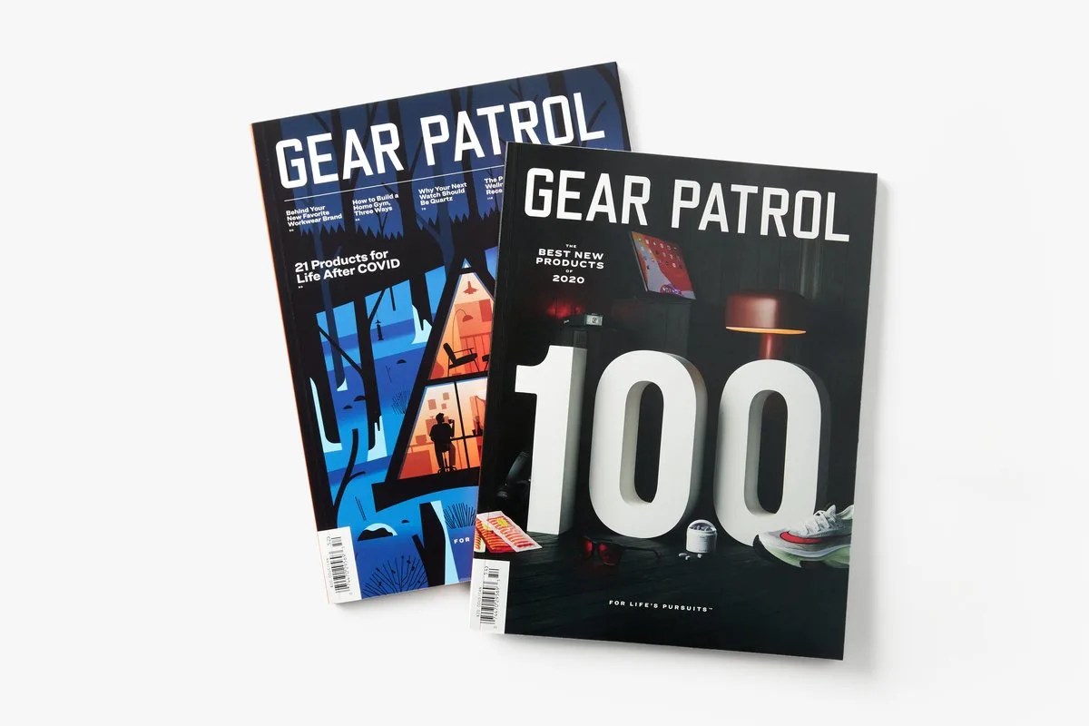 two copies of gear patrol magazine issue fourteen with an a frame cabin on the cover, and issue fifteen with the numbers "100" on the cover