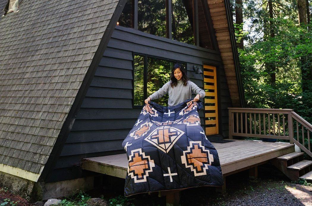 a woman shaking out an insulated blanket on a deck