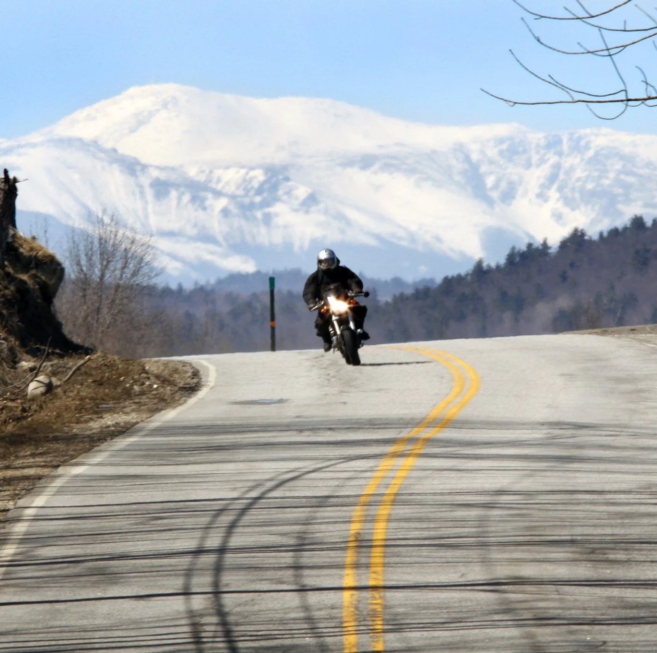 a snow covered mount washington looms large in the background as a motorcyclist rides over the crest