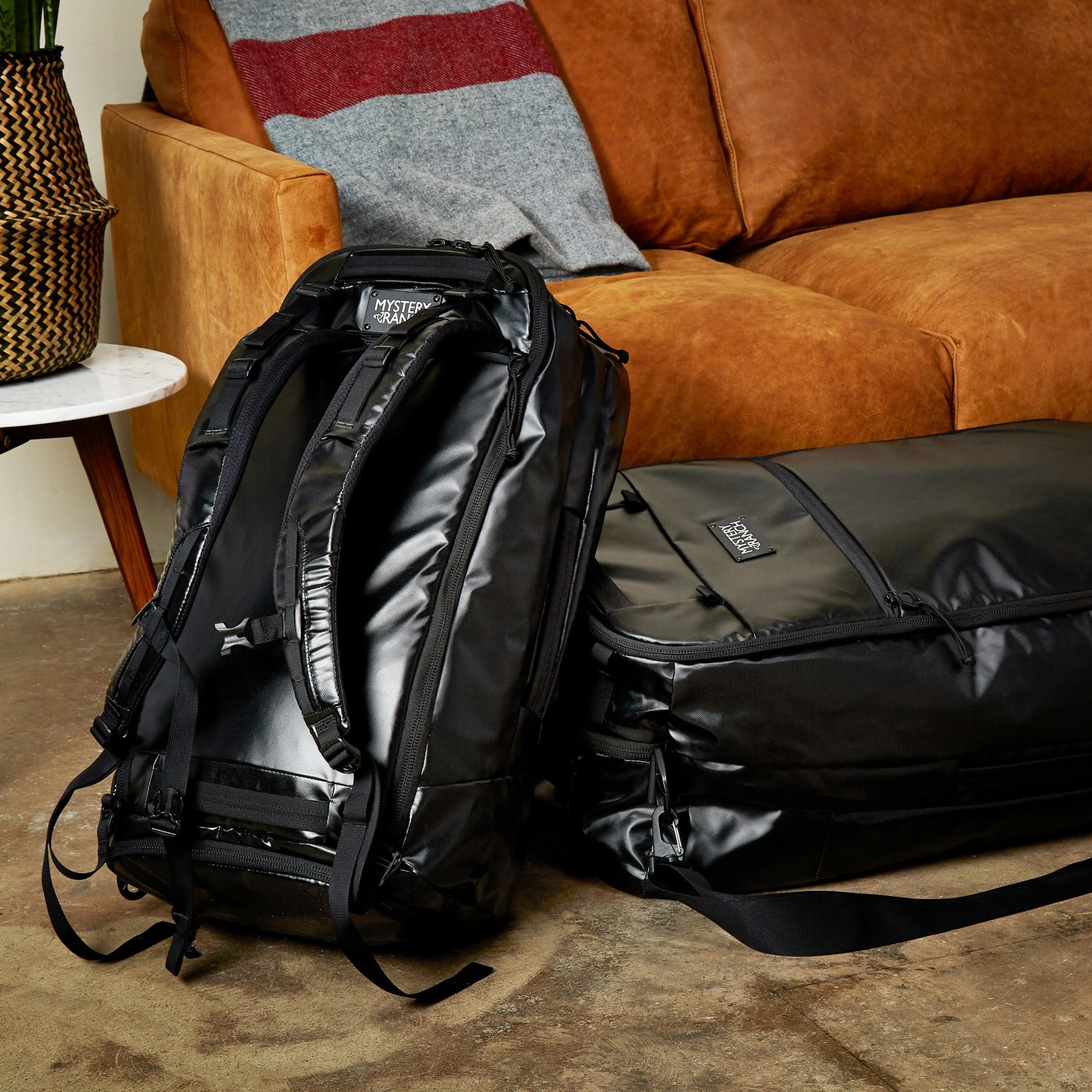 two black duffel bags on the floor near a couch