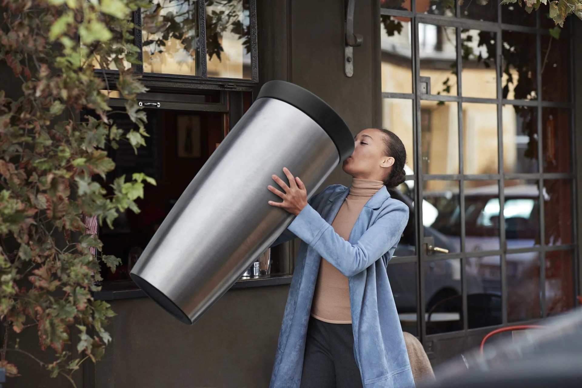 woman drinking coffee from large travel mug at take away counter of cafe